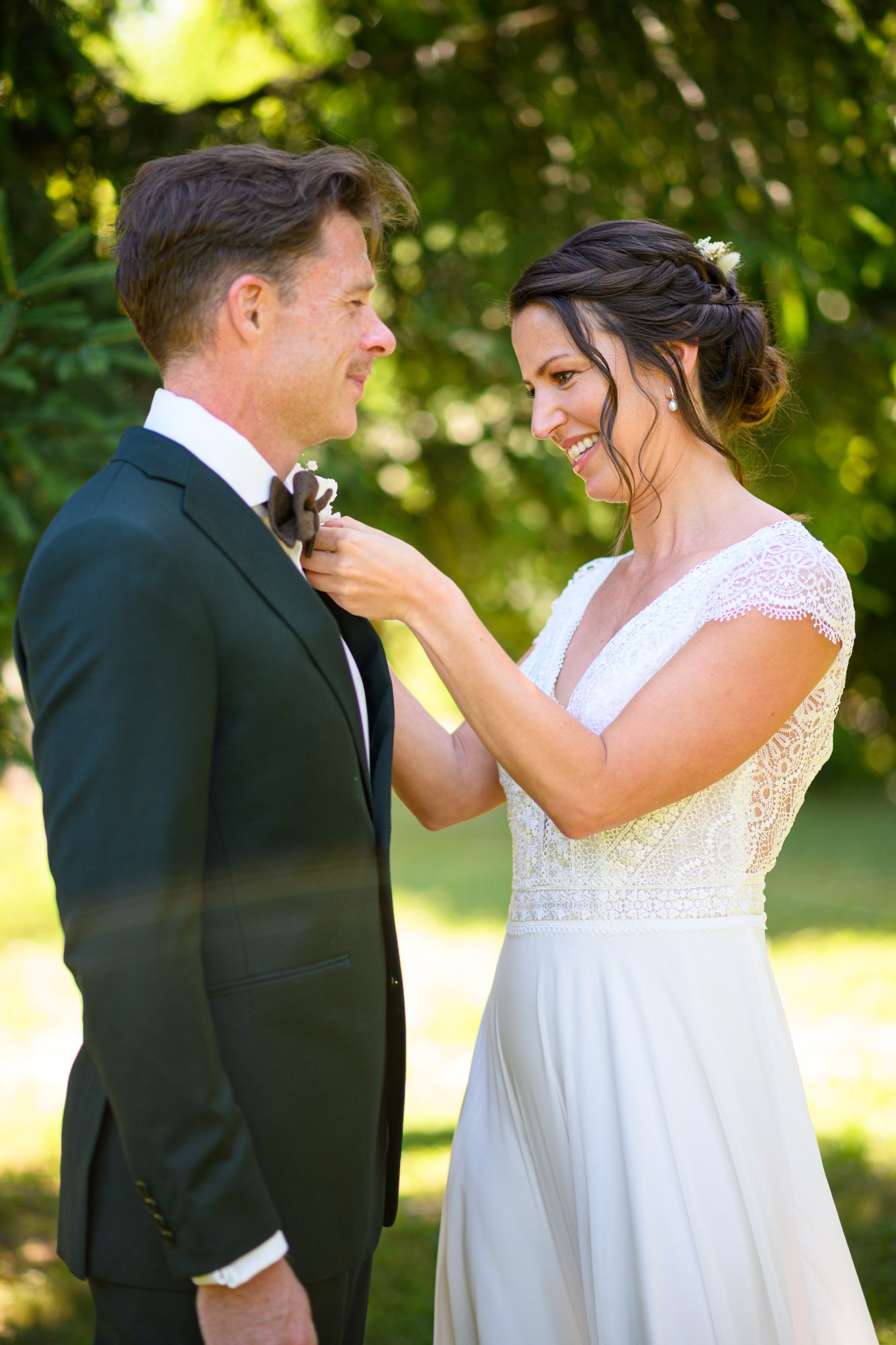 Un couple en tenue de mariage échange un regard tendre dans un cadre extérieur verdoyant.
