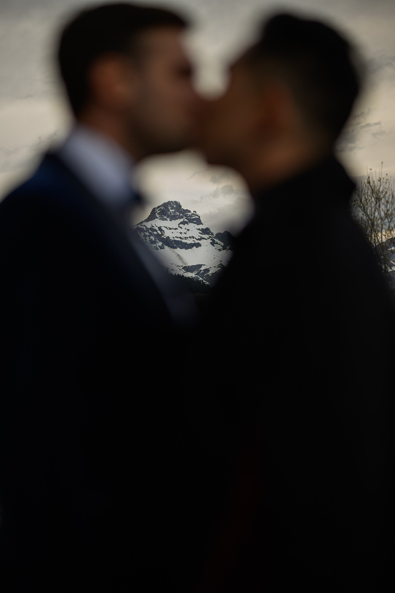 Deux hommes homosexuels s'embrassent, flous, avec une montagne enneigée en arrière-plan.