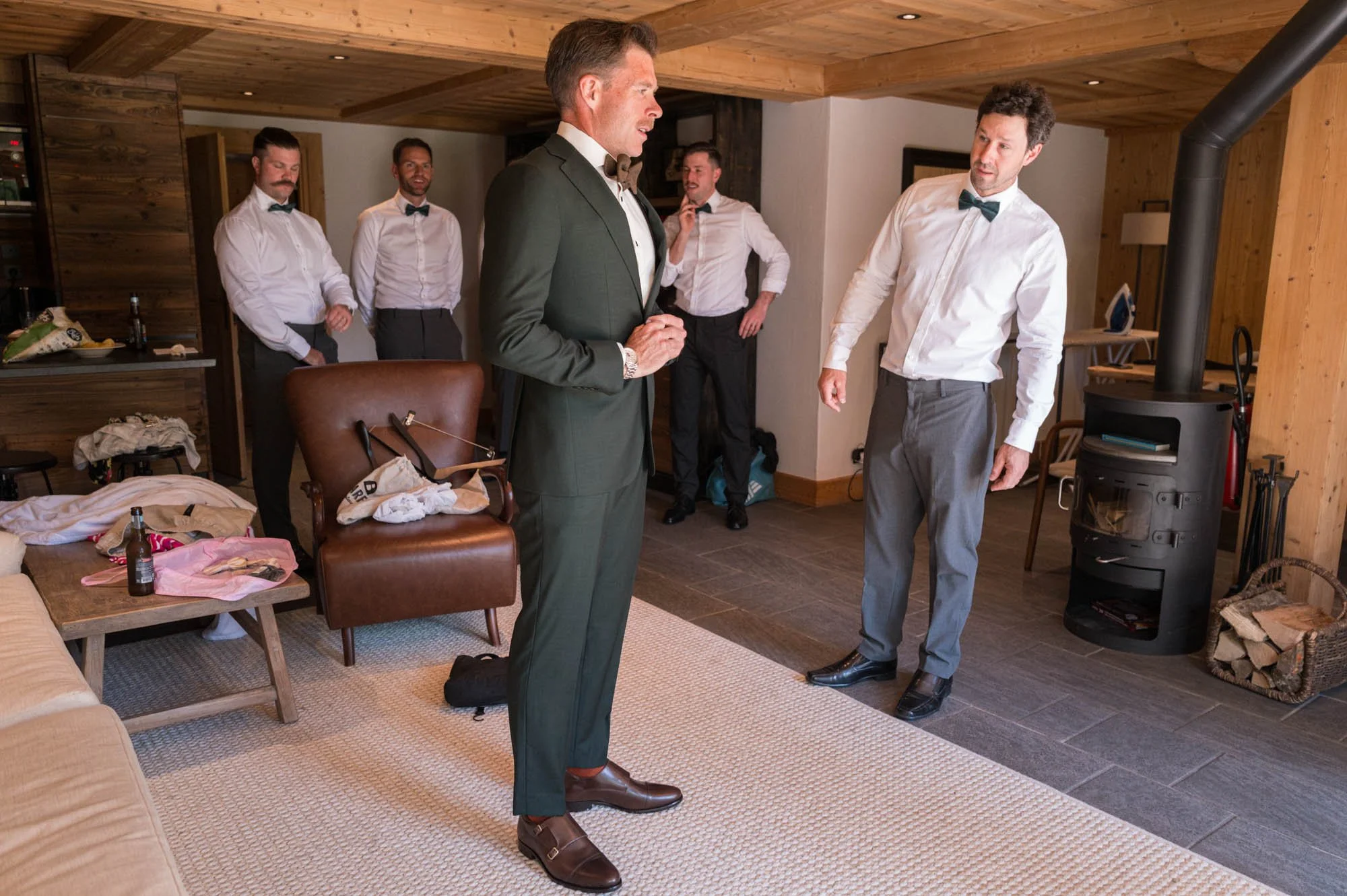 Un groupe de jeunes hommes en tenue formelle dans une pièce en bois, en train de se préparer pour une occasion spéciale, probablement un mariage.