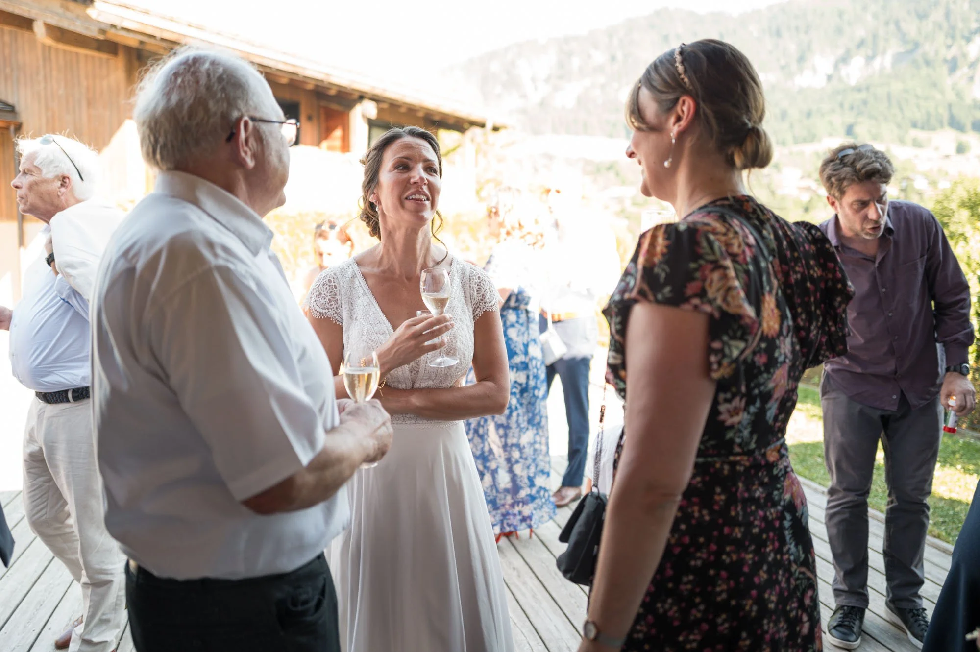 Groupe de personnes discutant lors d'une réception en plein air, avec une maison en bois en arrière-plan et un paysage de montagne.