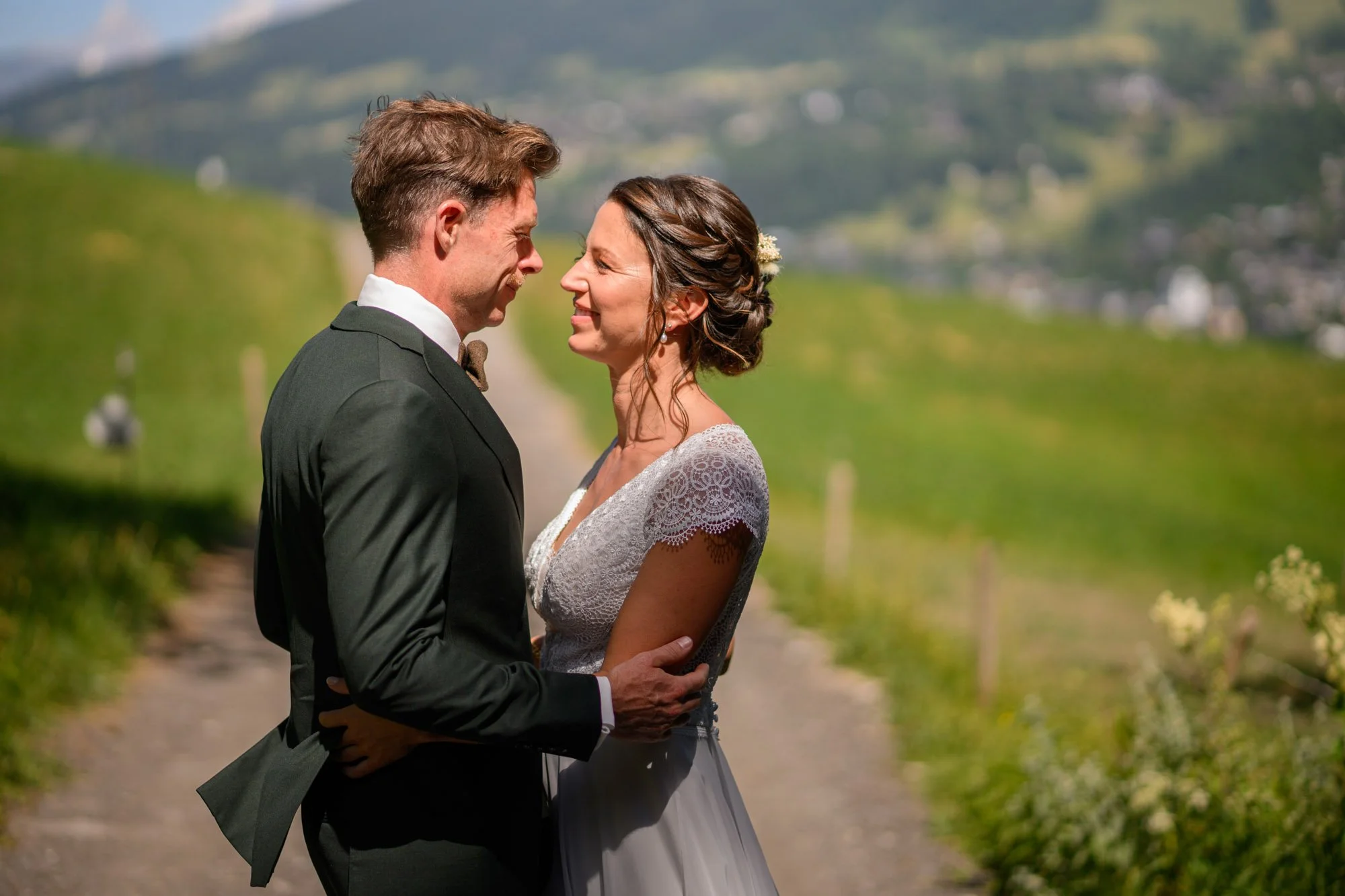 Un couple de mariés en tenue de mariage se regardant tendrement dans un paysage rural lors d'une journée ensoleillée.