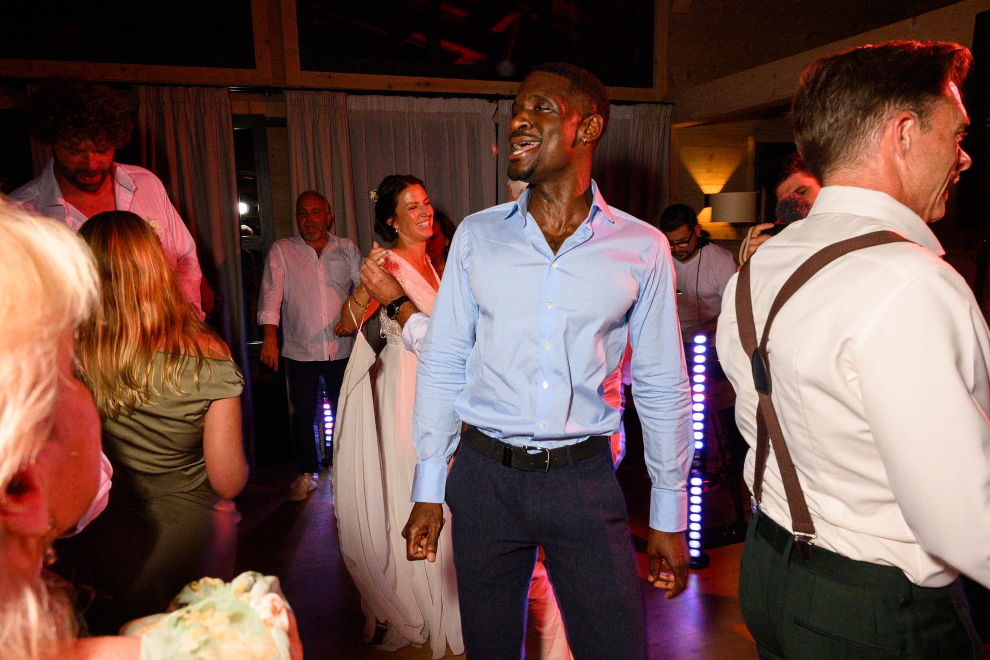 Groupe de personnes dansant et souriant lors d'une fête ou d'un événement social, ambiance joyeuse, éclairage tamisé, intérieur chaleureux.