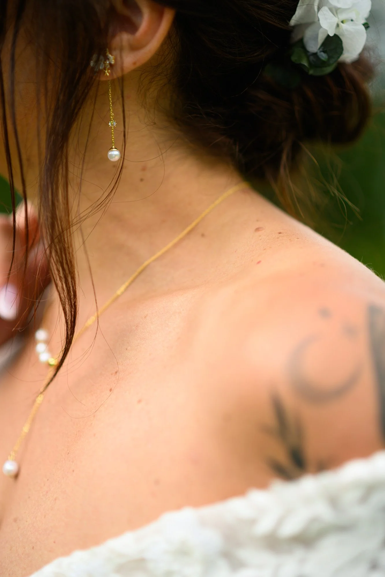 Close-up d'une femme portant des bijoux dorés et des fleurs dans les cheveux, montrant une épaule tatouée.