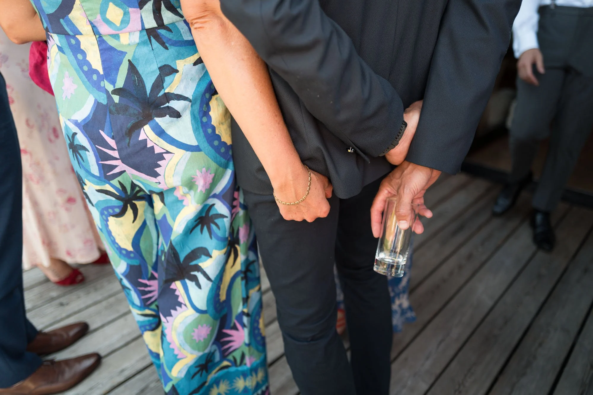 Personne tenant un verre vide en réunion ou événement social, avec d'autres personnes présentes en arrière-plan.