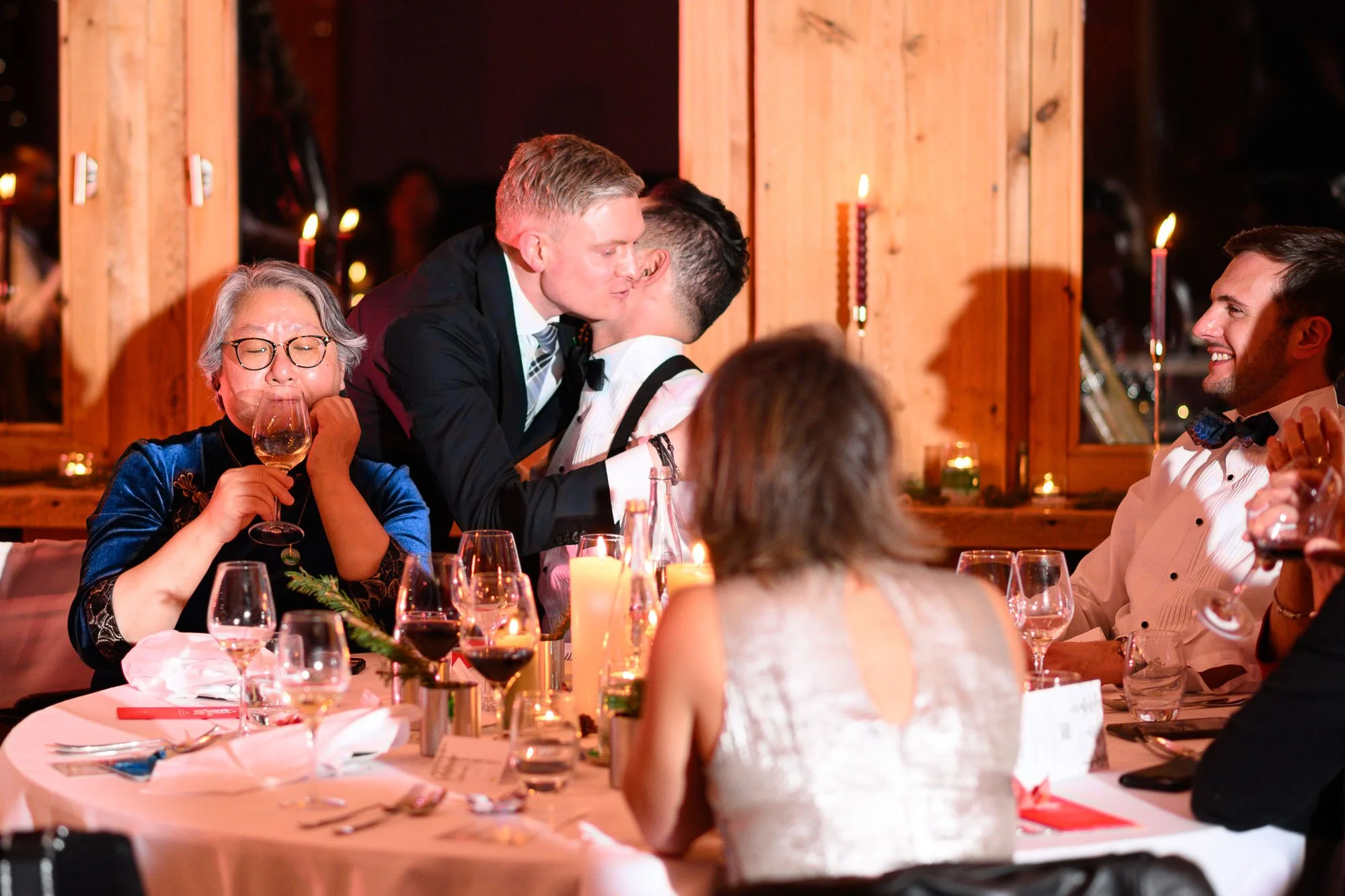 Un groupe de personnes à une fête ou un dîner, célébrant avec des verres de vin et des sourires, dans une ambiance chaleureuse avec des bougies et une décoration en bois.