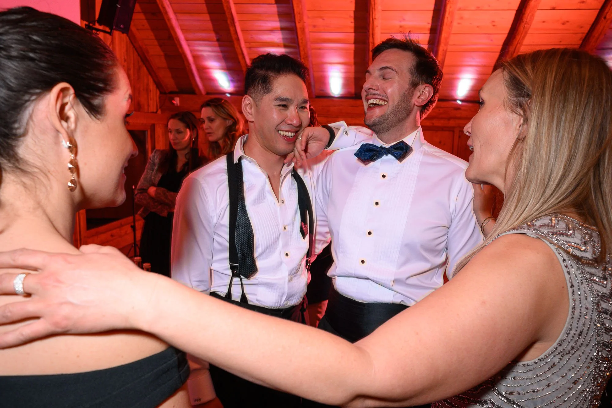 Groupe de personnes qui sourient et s'embrassent lors d'une fête dans un chalet en bois, ambiance chaleureuse et conviviale.