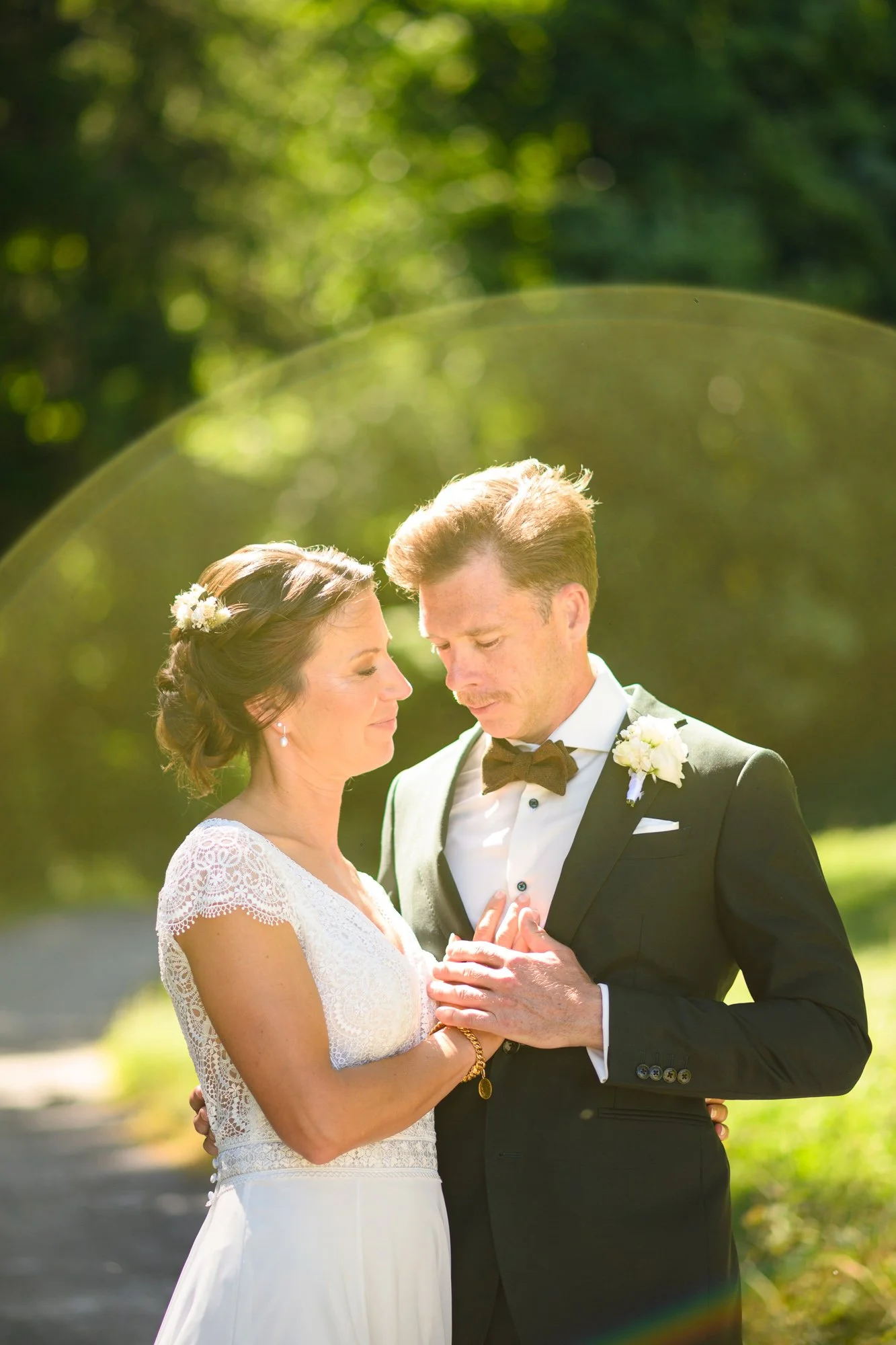 Un couple de mariés lors de leur mariage en plein air, avec un fond de nature verdoyante, se tenant près les yeux fermés, en tenue de mariage.
