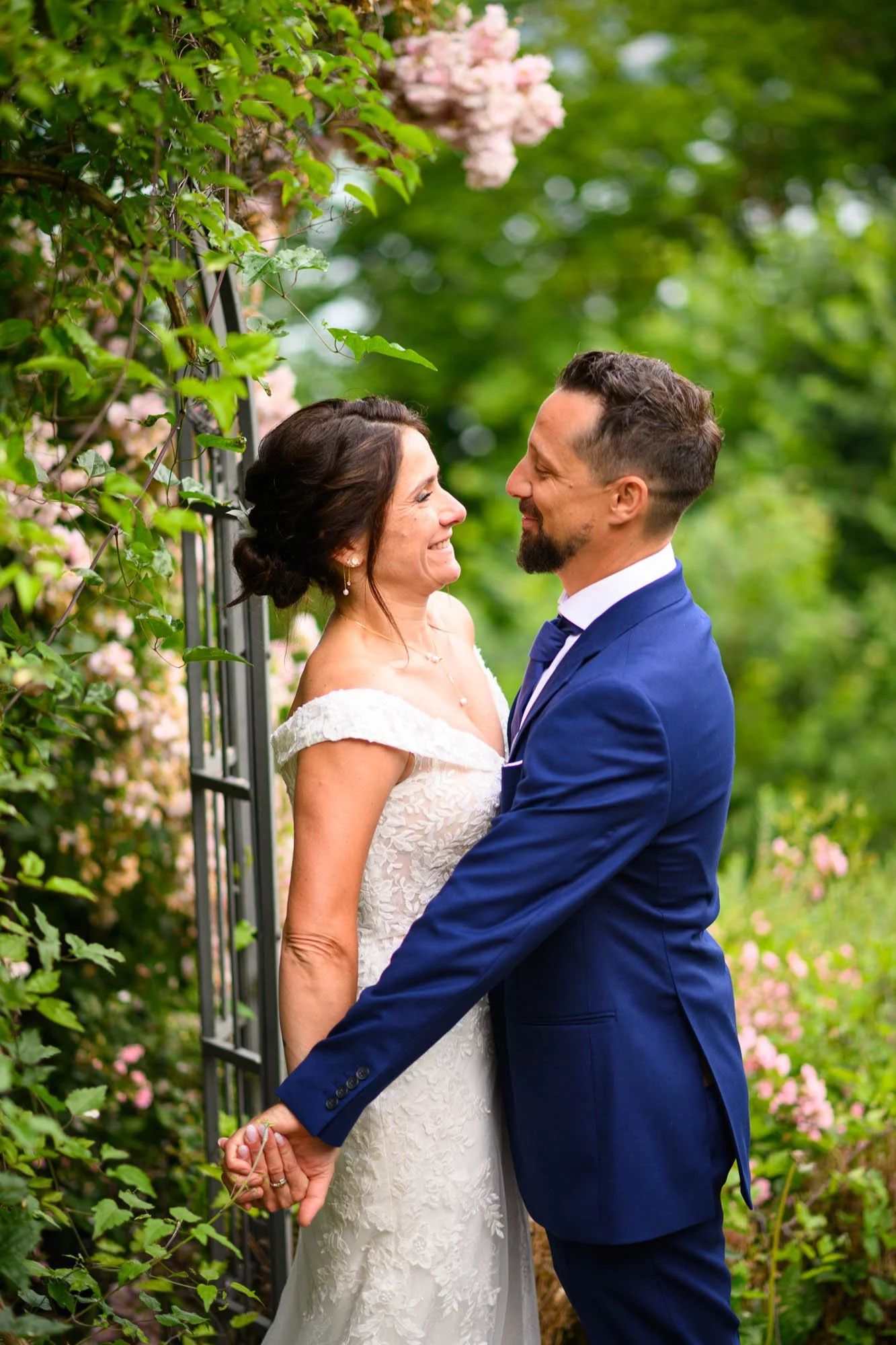 Un couple de mariés regardant avec amour dans un jardin entouré de fleurs.