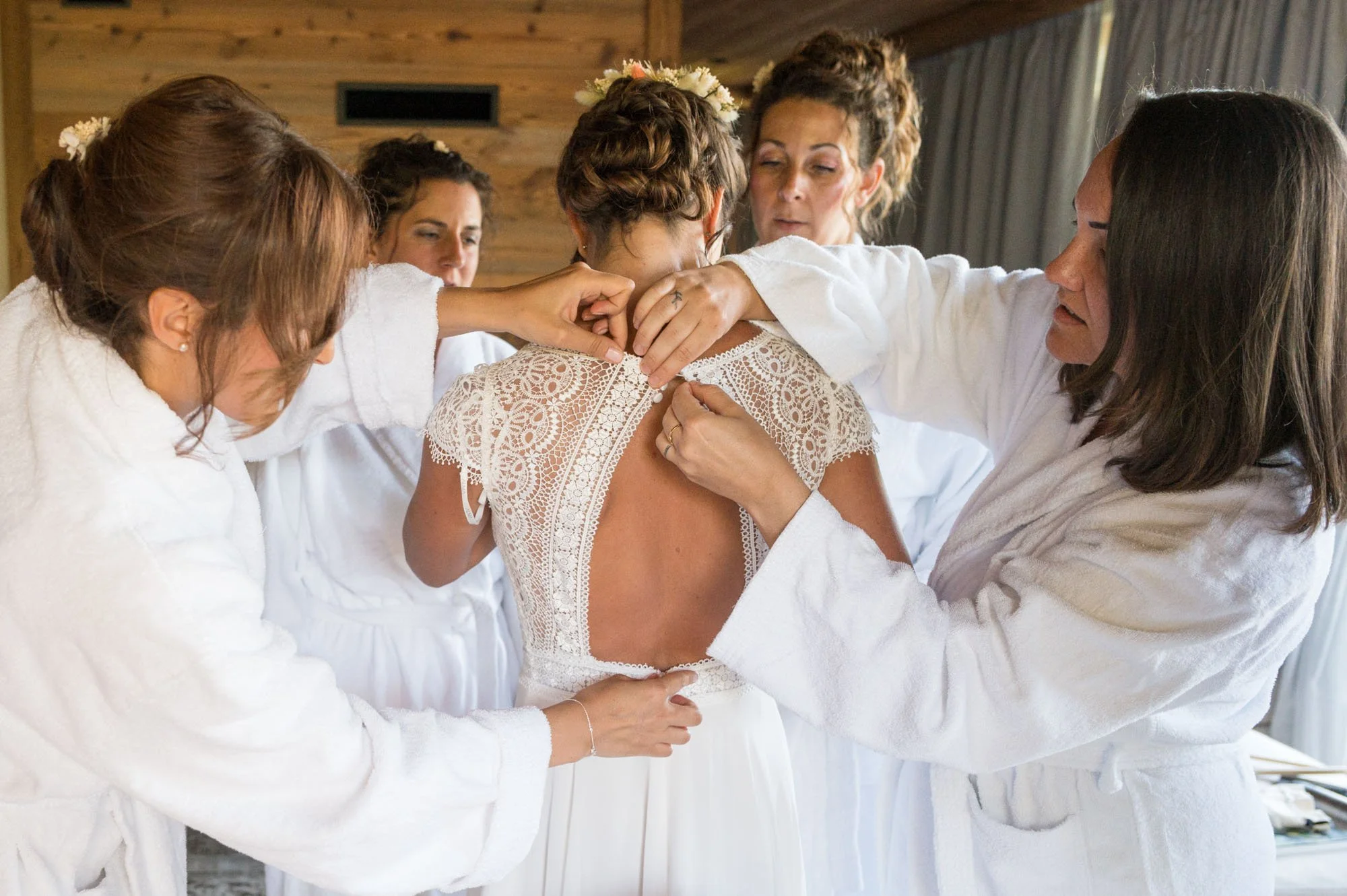 Femmess en peignoir blanc aidant une mariée à attacher sa robe de mariée.