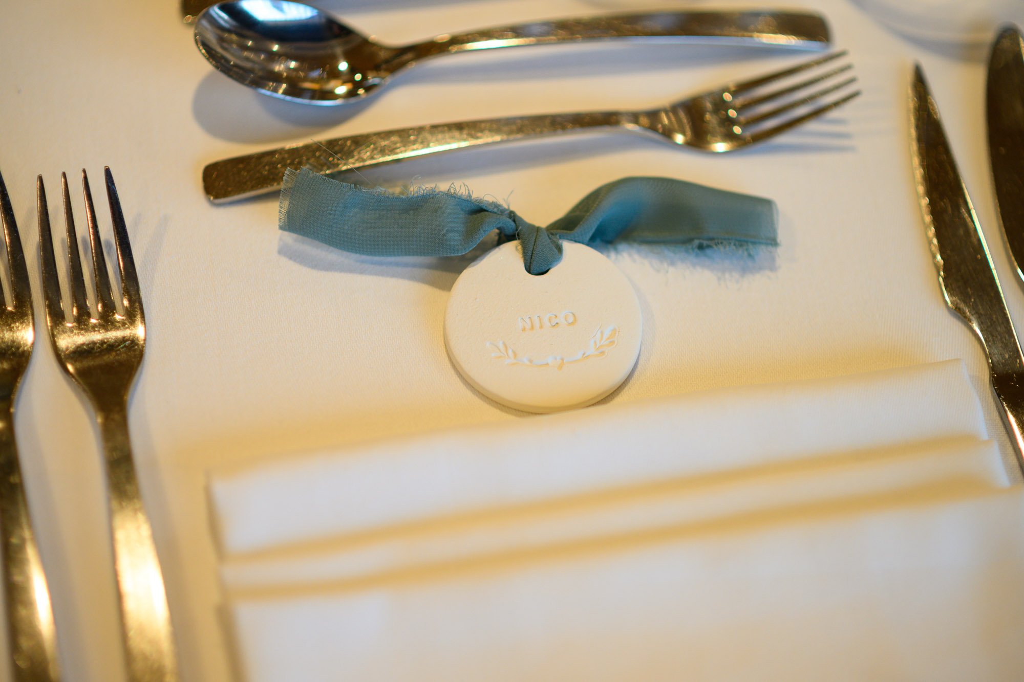 Cadeau de mariage personnalisé avec le nom 'Nico' attaché à une nappe de table blanche, entouré de couverts en argent, pour une réception élégante.