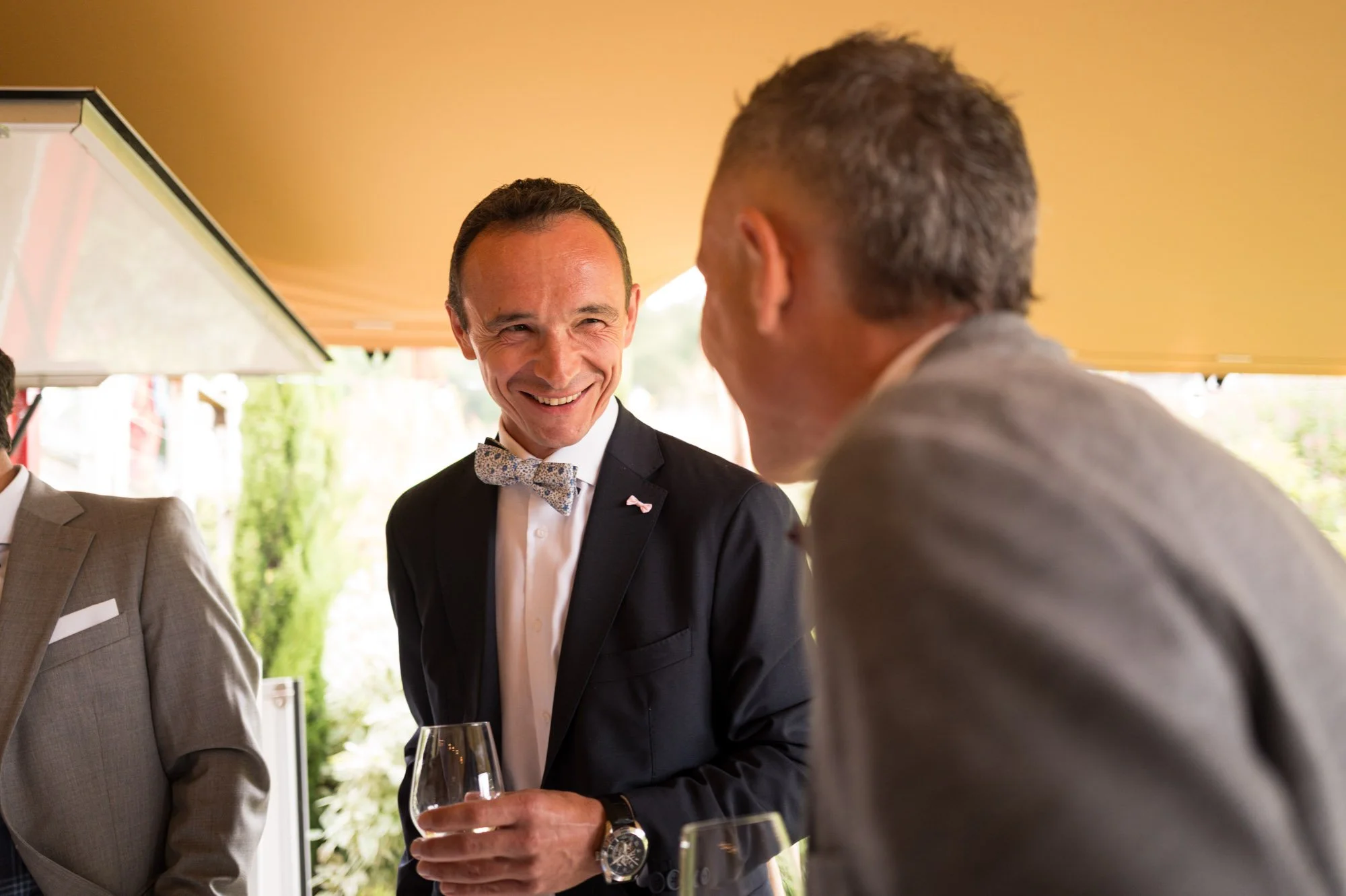 Deux hommes habillés en costume conversent lors d'une réception ou d'un dîner, l'un d'eux souriant.