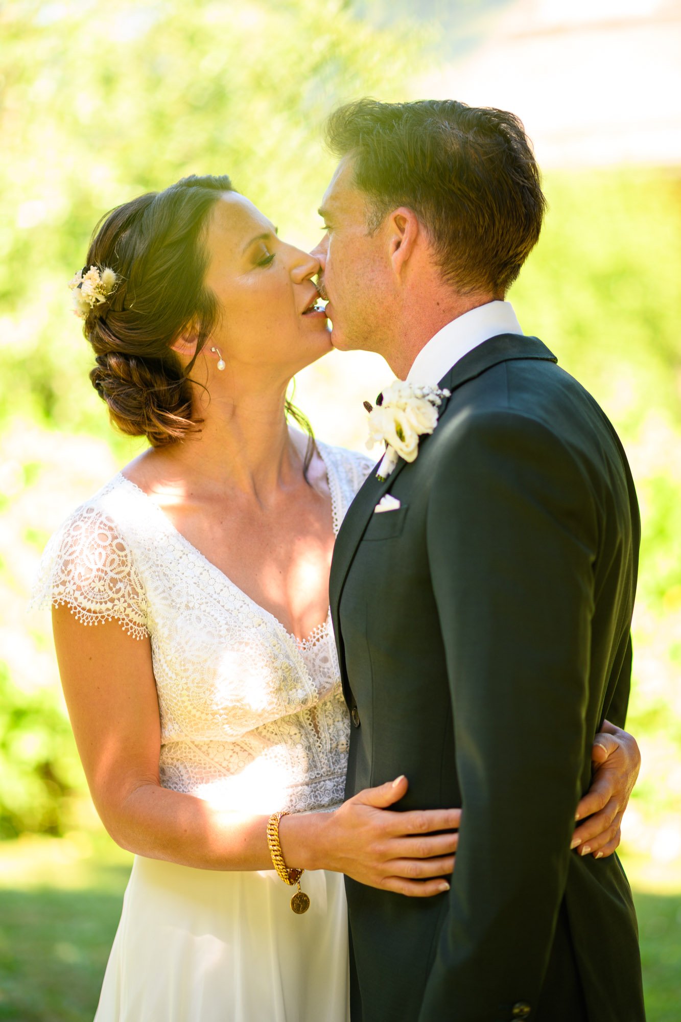 Un couple de mariés s'embrassant lors d'un mariage en plein air, sous la lumière du soleil.