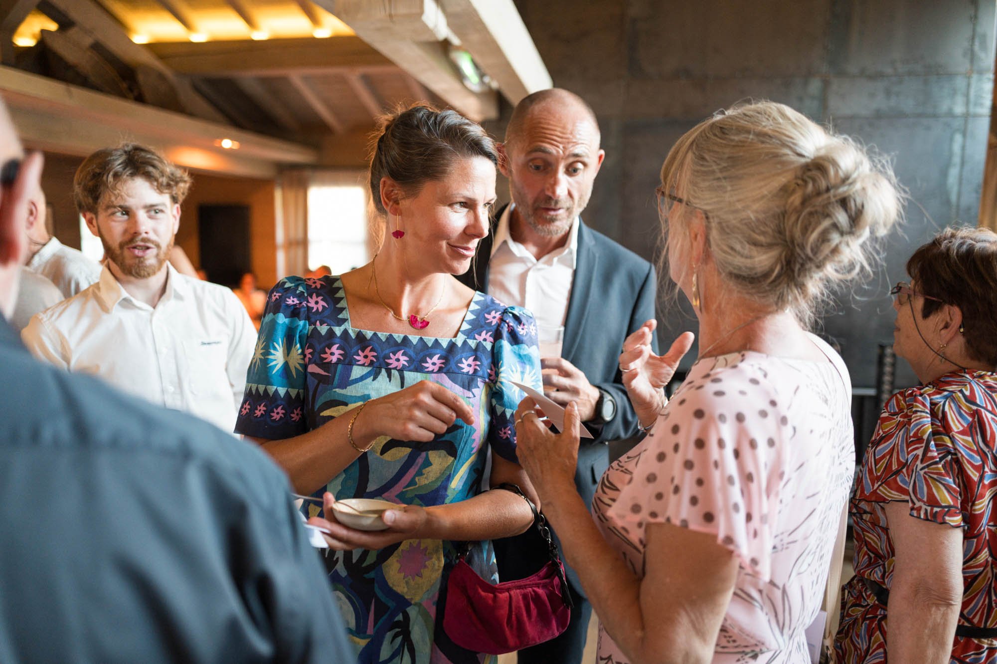 Groupe de personnes en conversation lors d'une réception ou d'une événement social, intérieur chaleureux avec lumière naturelle
