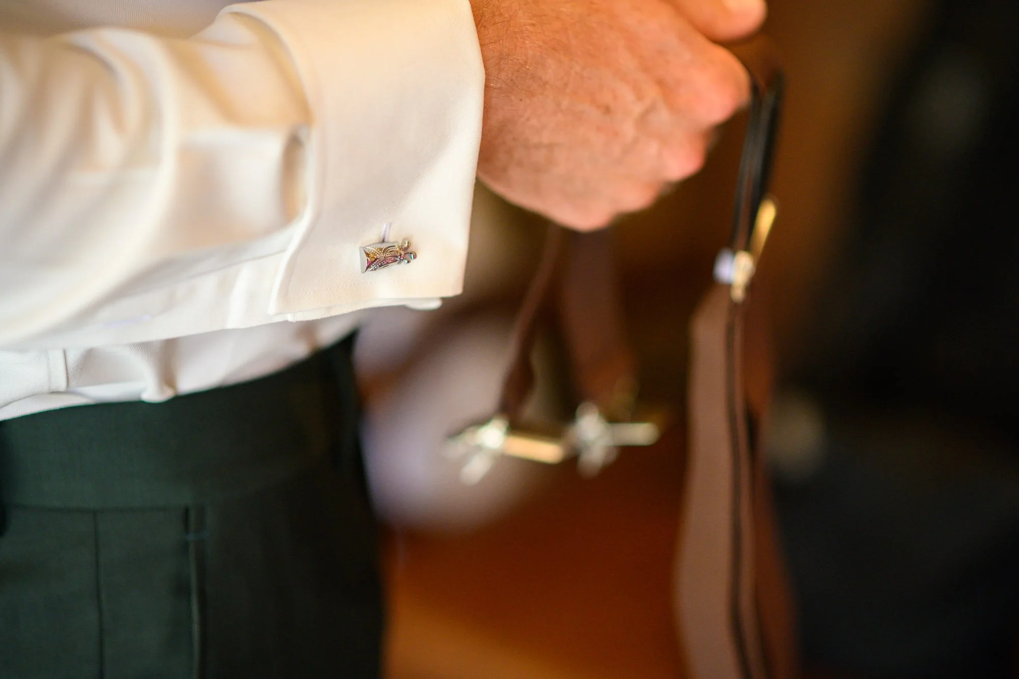 Détail d'une femme portant une chemise blanche avec un bijou épinglé à la manche, et une montre en or sur le poignet.