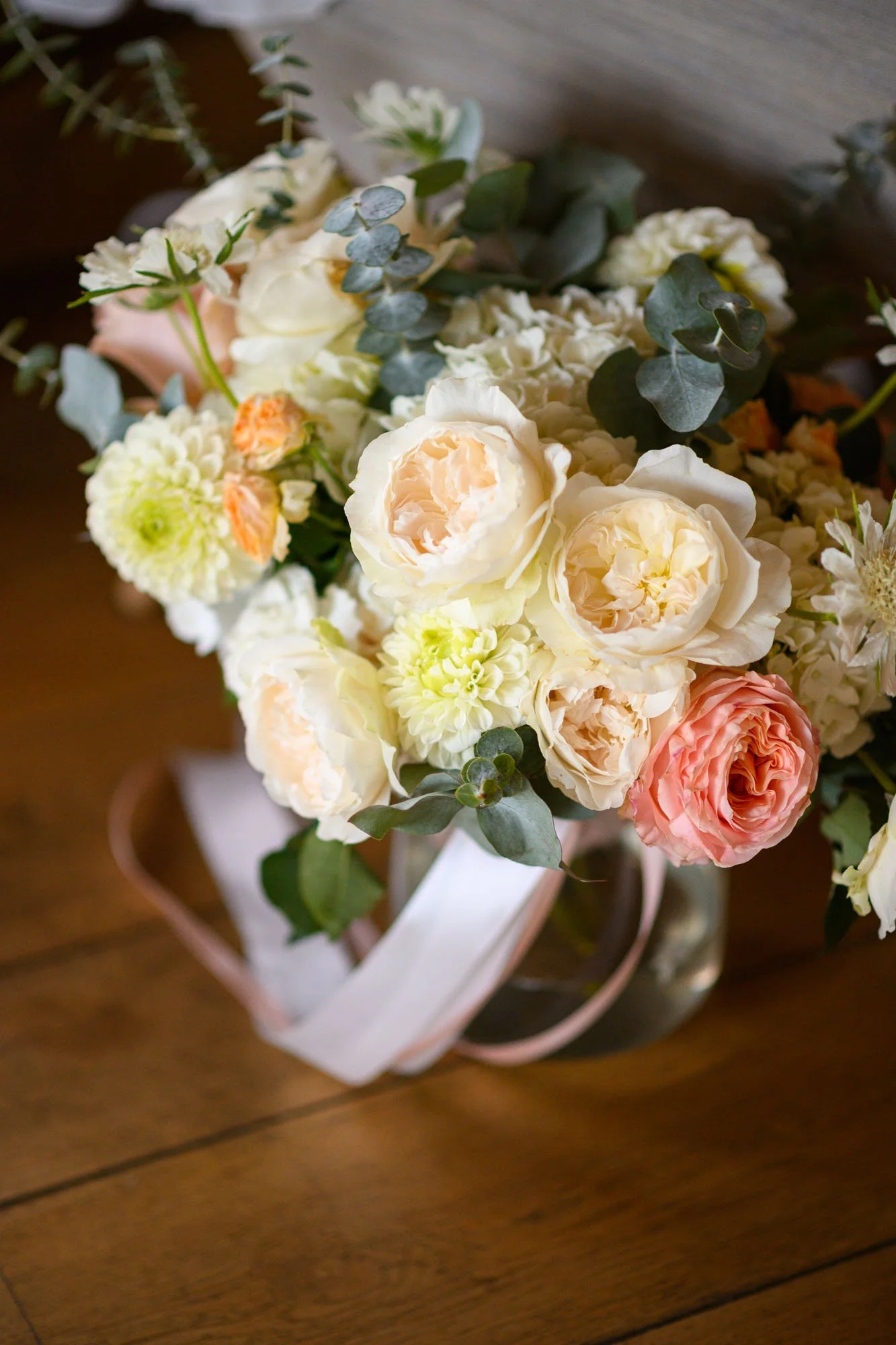 Un bouquet de fleurs blanches et roses avec des feuillages verts dans un vase en verre sur une table en bois.
