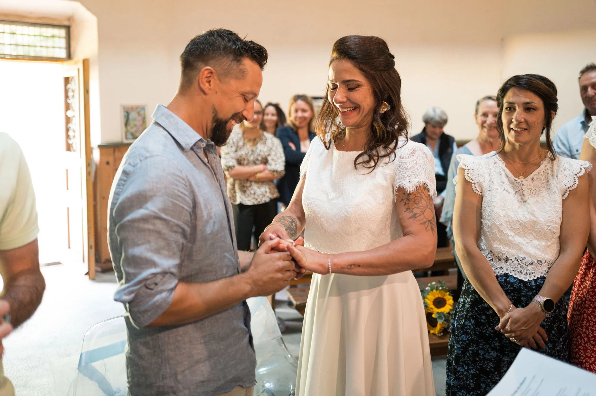 Un couple en train de s'échanger leurs vœux de mariage lors d'une cérémonie, entourés de proches souriants.