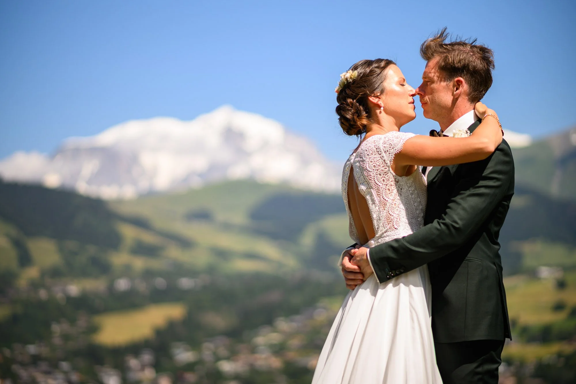 Un couple de mariés en étreinte lors d'un mariage en extérieur avec un paysage de montagnes et de verdure en arrière-plan.