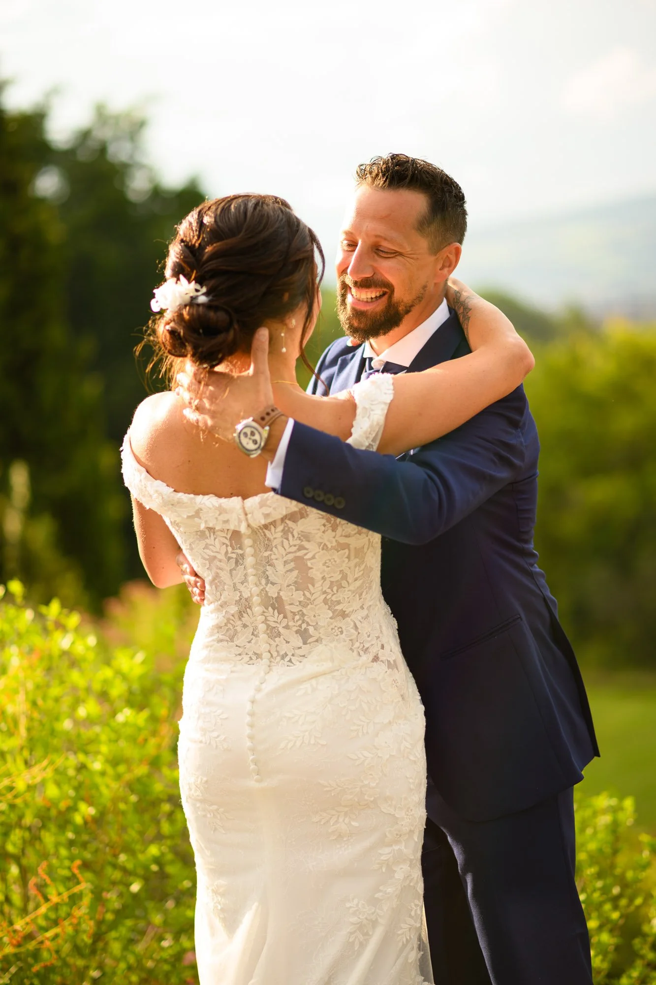 Un couple en tenue de mariage s'embrassant dans un extérieur verdoyant, en plein jour.
