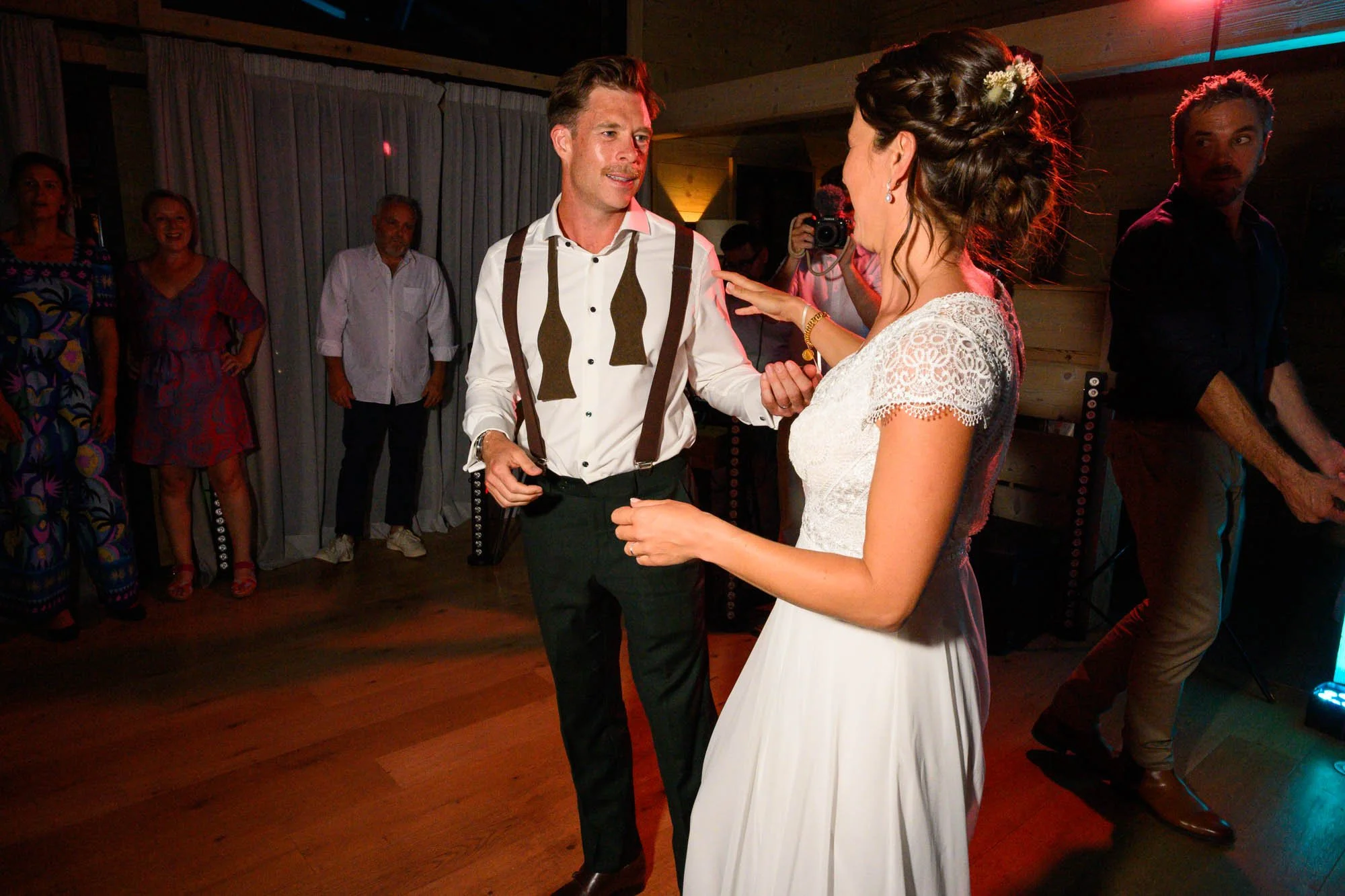 Un couple danse lors de leur mariage, avec des invités en arrière-plan, dans une salle décorée