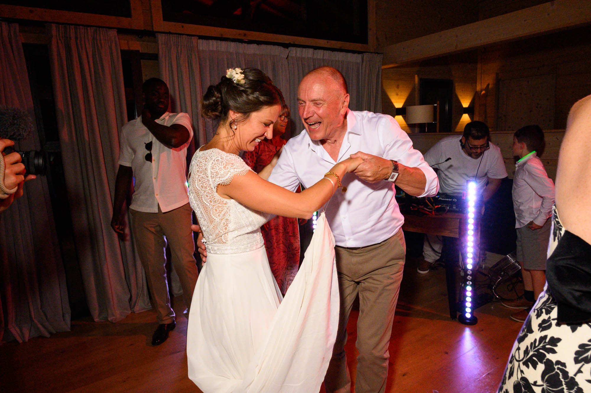 Un couple danse lors d'un mariage, la femme porte une robe blanche et l'homme un chemisier blanc, tous deux souriants.