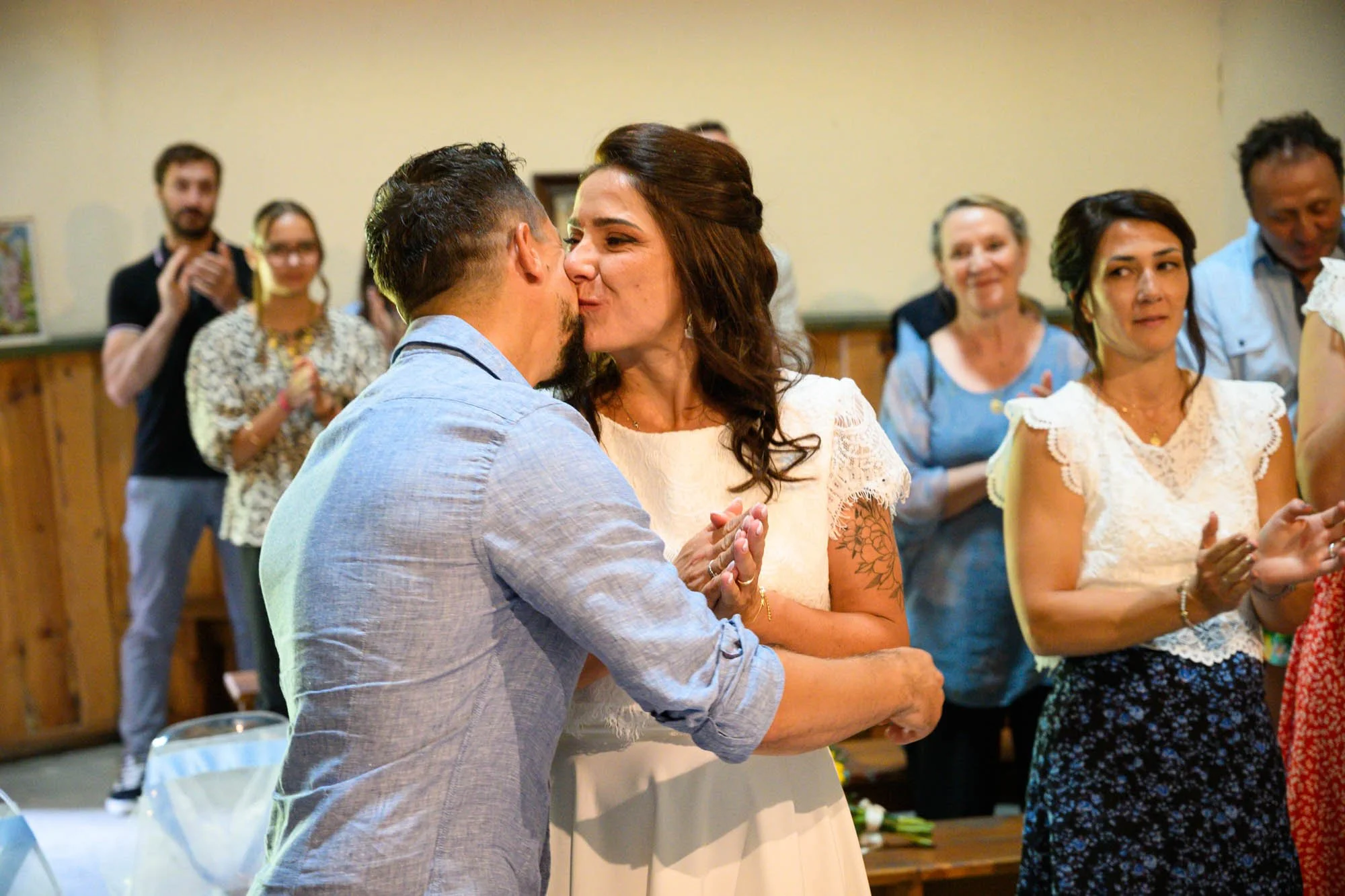 Un couple s'embrassant lors d'une cérémonie, d'autres personnes applaudissant dans une salle.