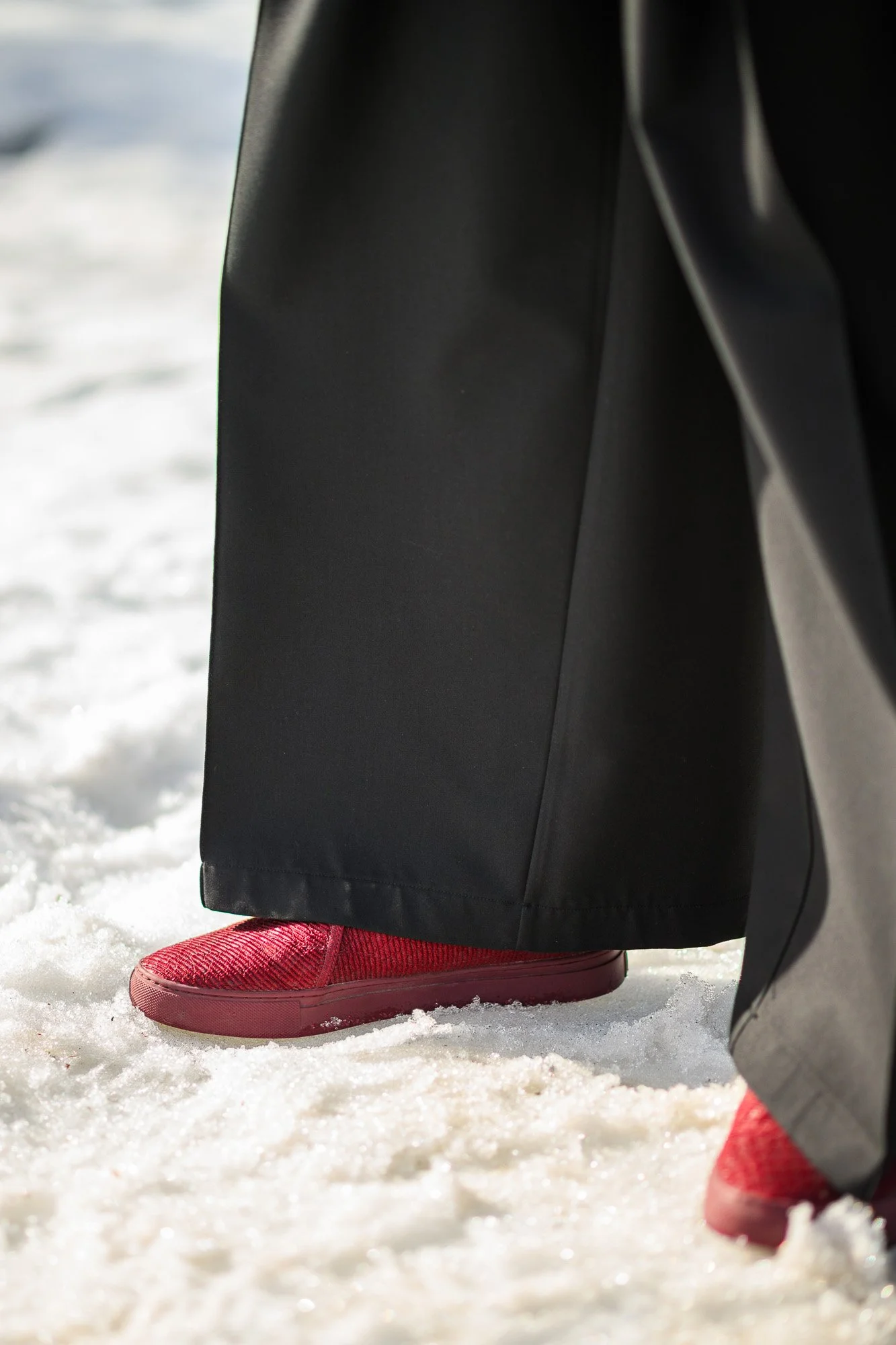 Une personne portant des chaussures de sport rouges et un pantalon noir marche dans la neige.