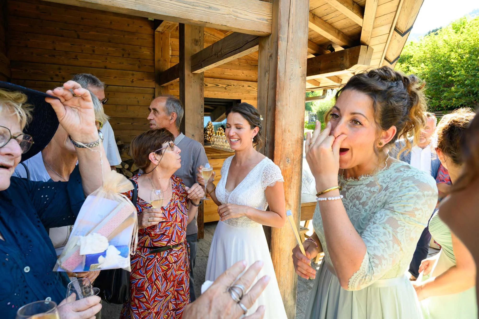 Groupe de personnes lors d'une célébration en plein air, la mariée en robe blanche souriante au centre, entourée de femmes et d'hommes discutant et riant.