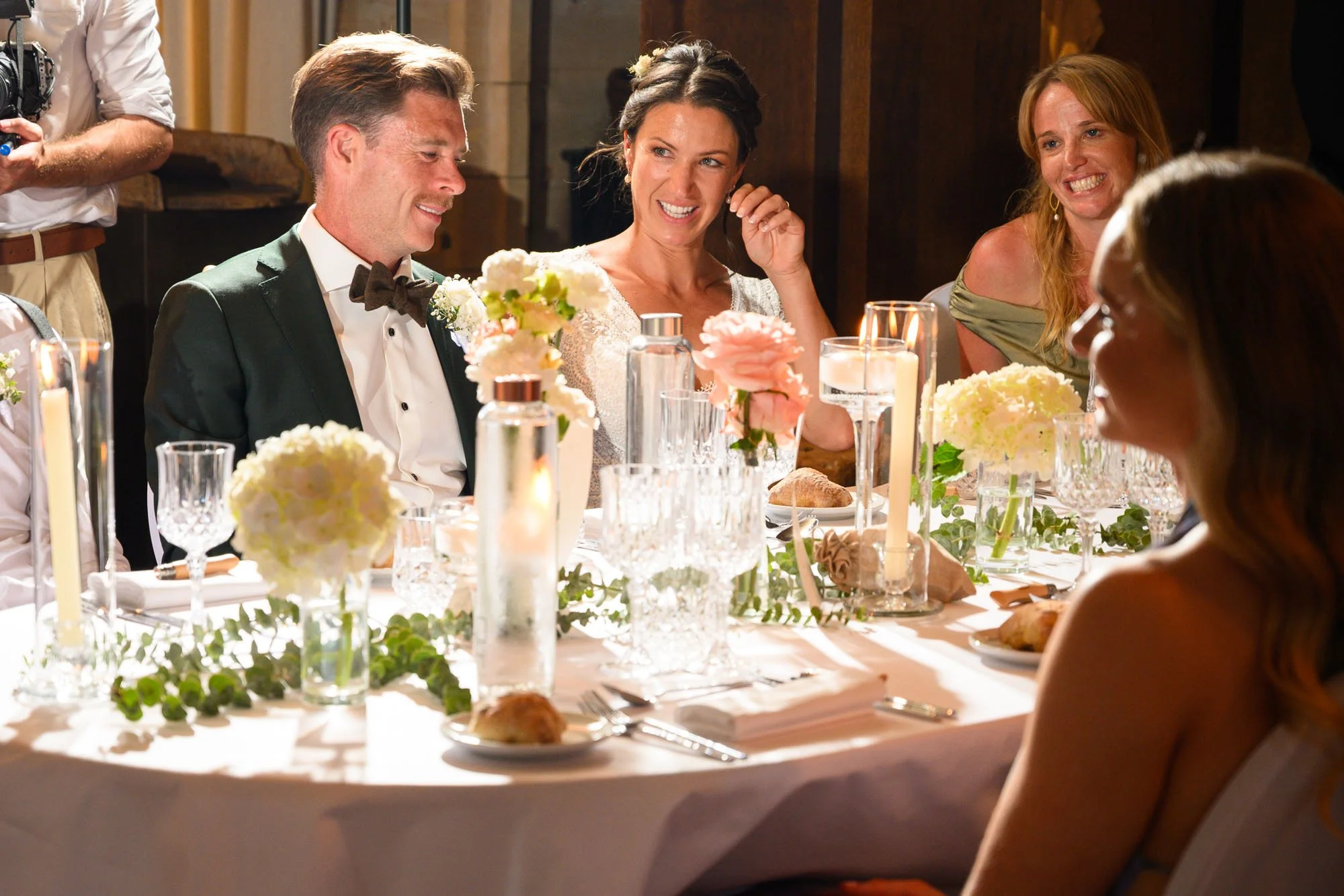 Groupe de personnes assises autour d'une table lors d'un repas de mariage, décorée de fleurs et de bougies.