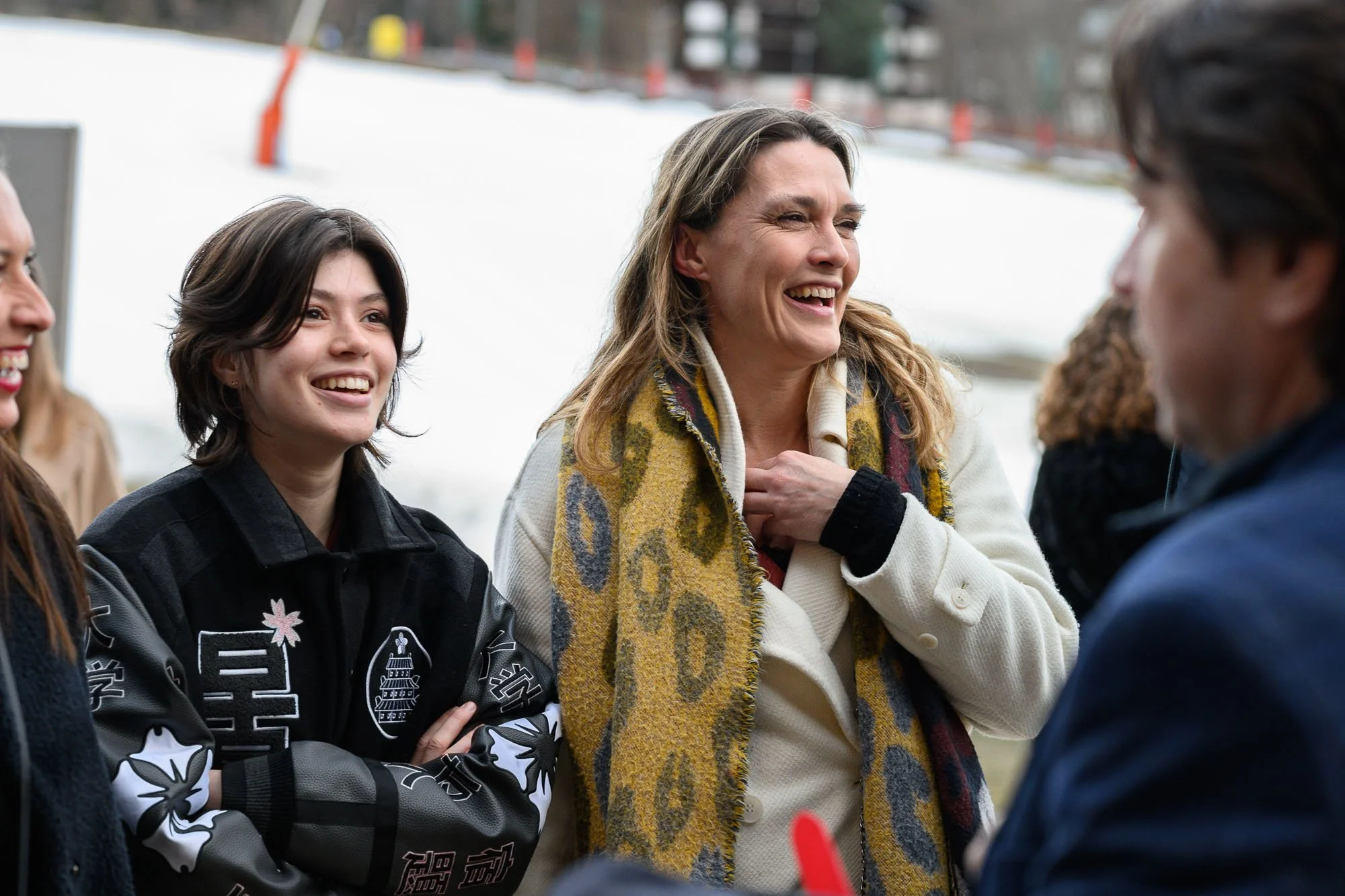 Groupe de quatre personnes d'âge adulte, souriant et discutant en extérieur, avec un décor enneigé en arrière-plan.