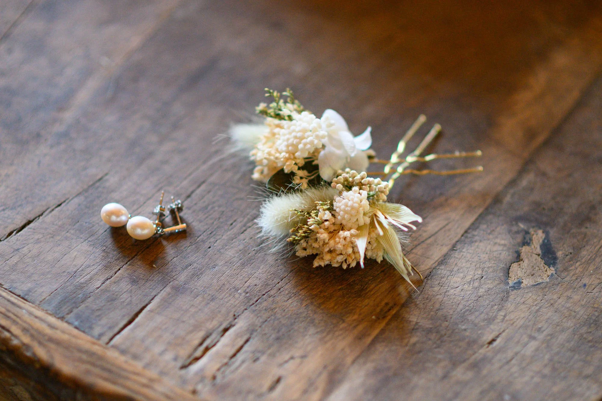 Boucles d'oreilles en perles et pince à cheveux avec fleurs blanches sur une table en bois.