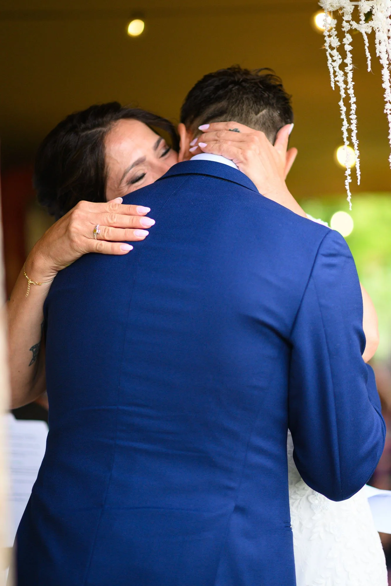 Deux personnes s'embrassent lors d'une cérémonie, une femme avec des mains ornées de bijoux embrassant un homme en costume bleu.