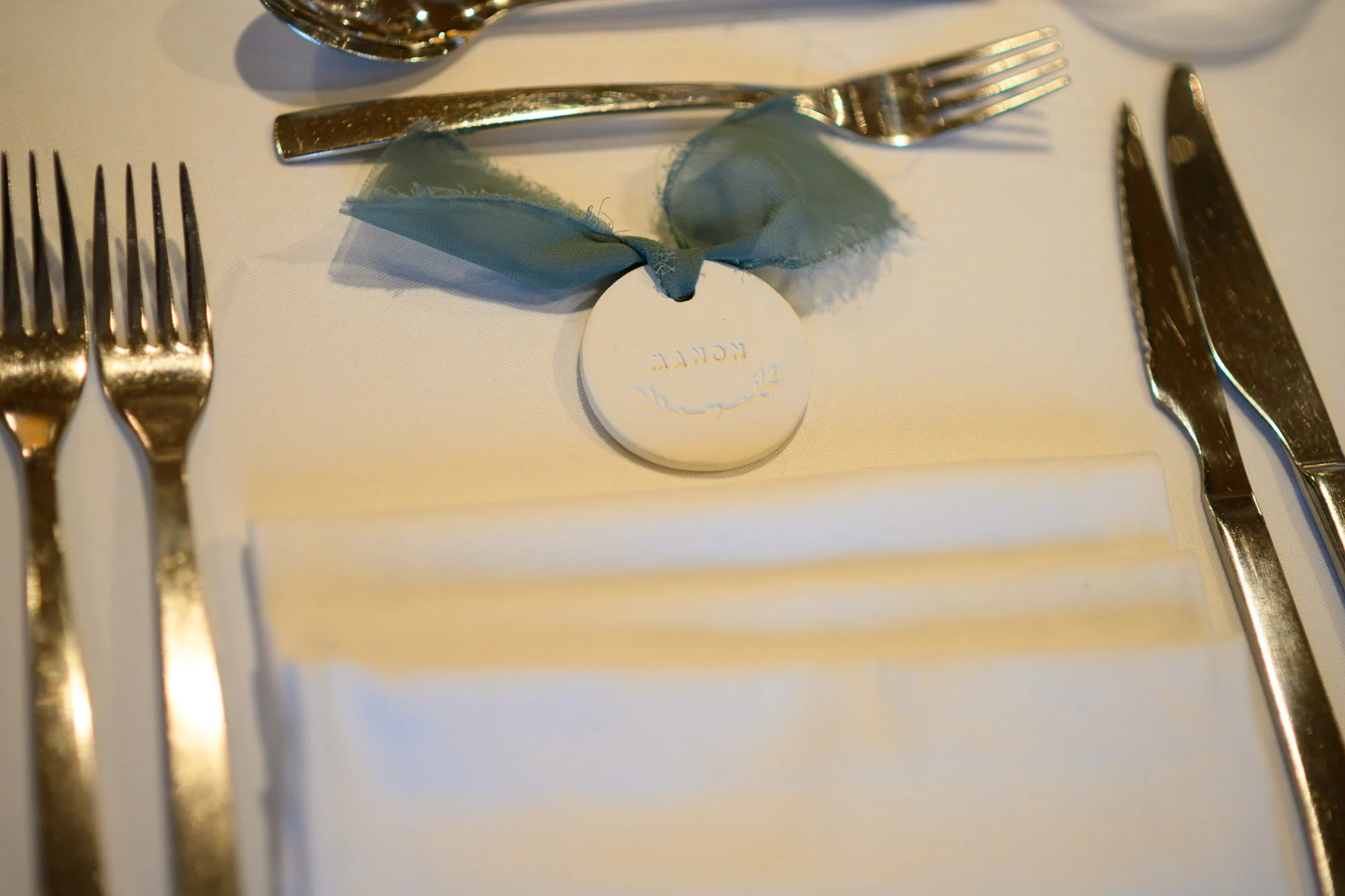 Couverts en argent, nappe blanche, bouton de mariage avec ruban en tissu bleu, inséré dans une nappe