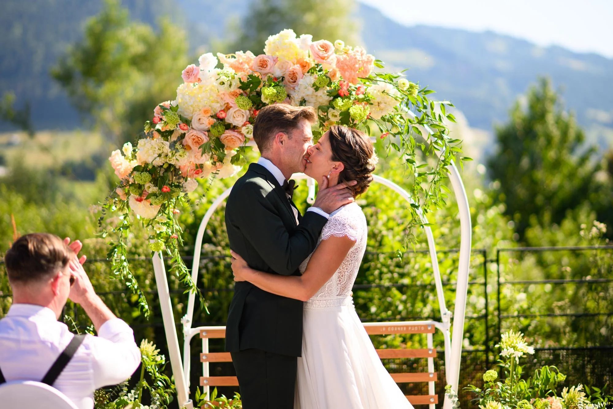 Un couple de mariés s'embrassant sous une arche de fleurs lors d'un mariage en plein air.
