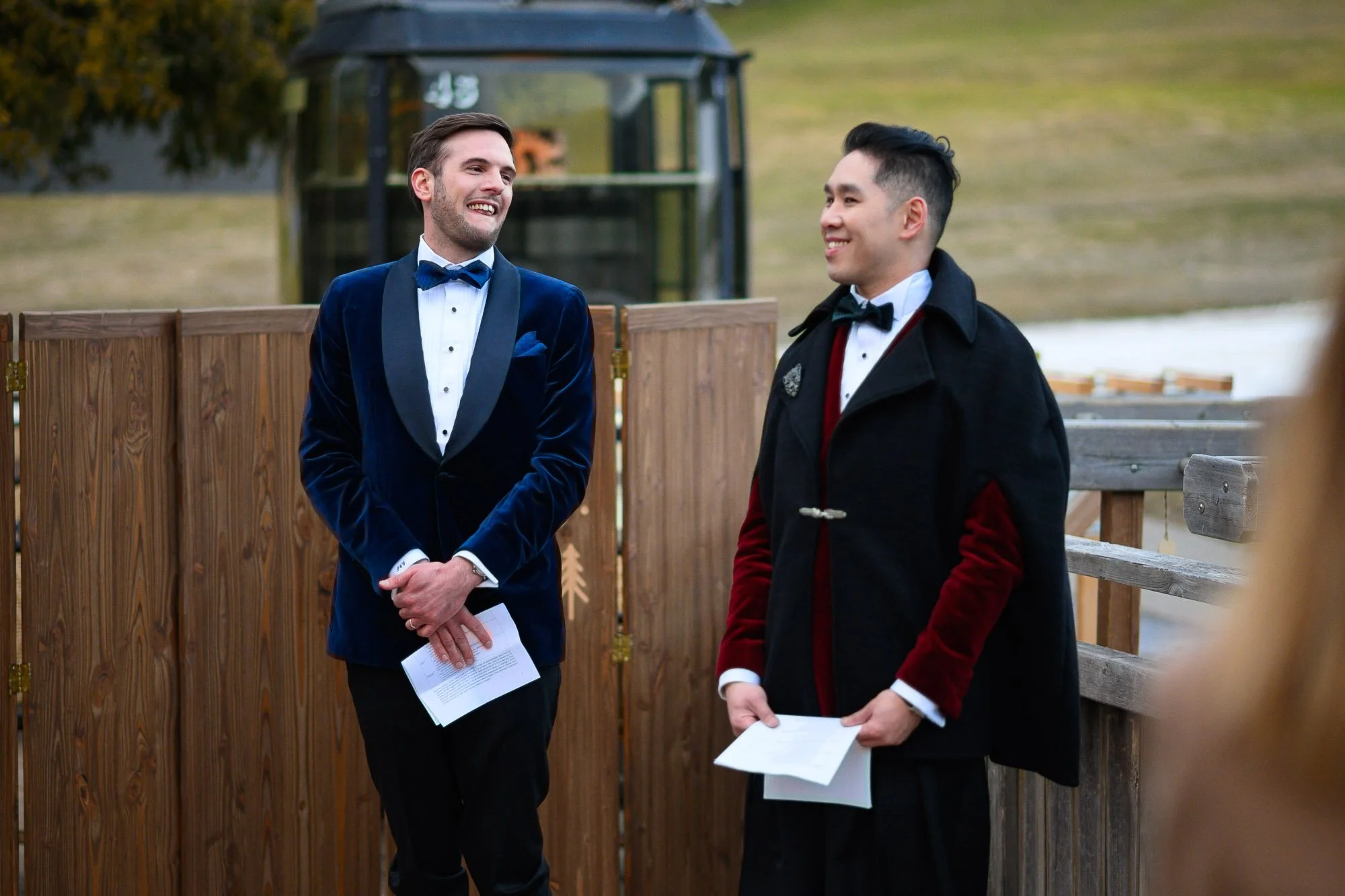 Deux hommes habillés en costumes lors d'une cérémonie en plein air, souriants et tenant des papiers.