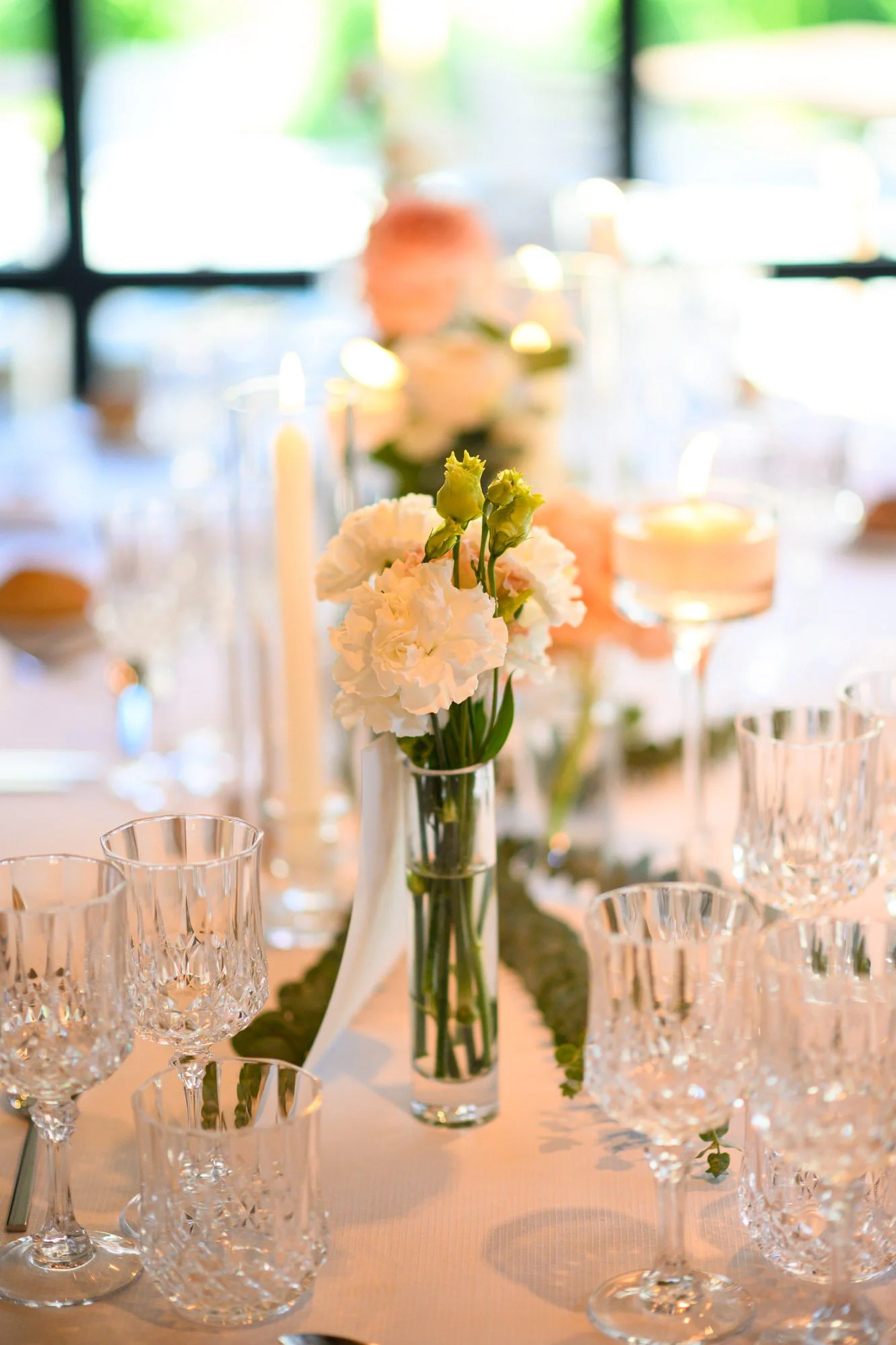 Centre de table avec des fleurs blanches dans un vase en verre, entouré de verres à vin en cristal sur une table préparée pour un événement.