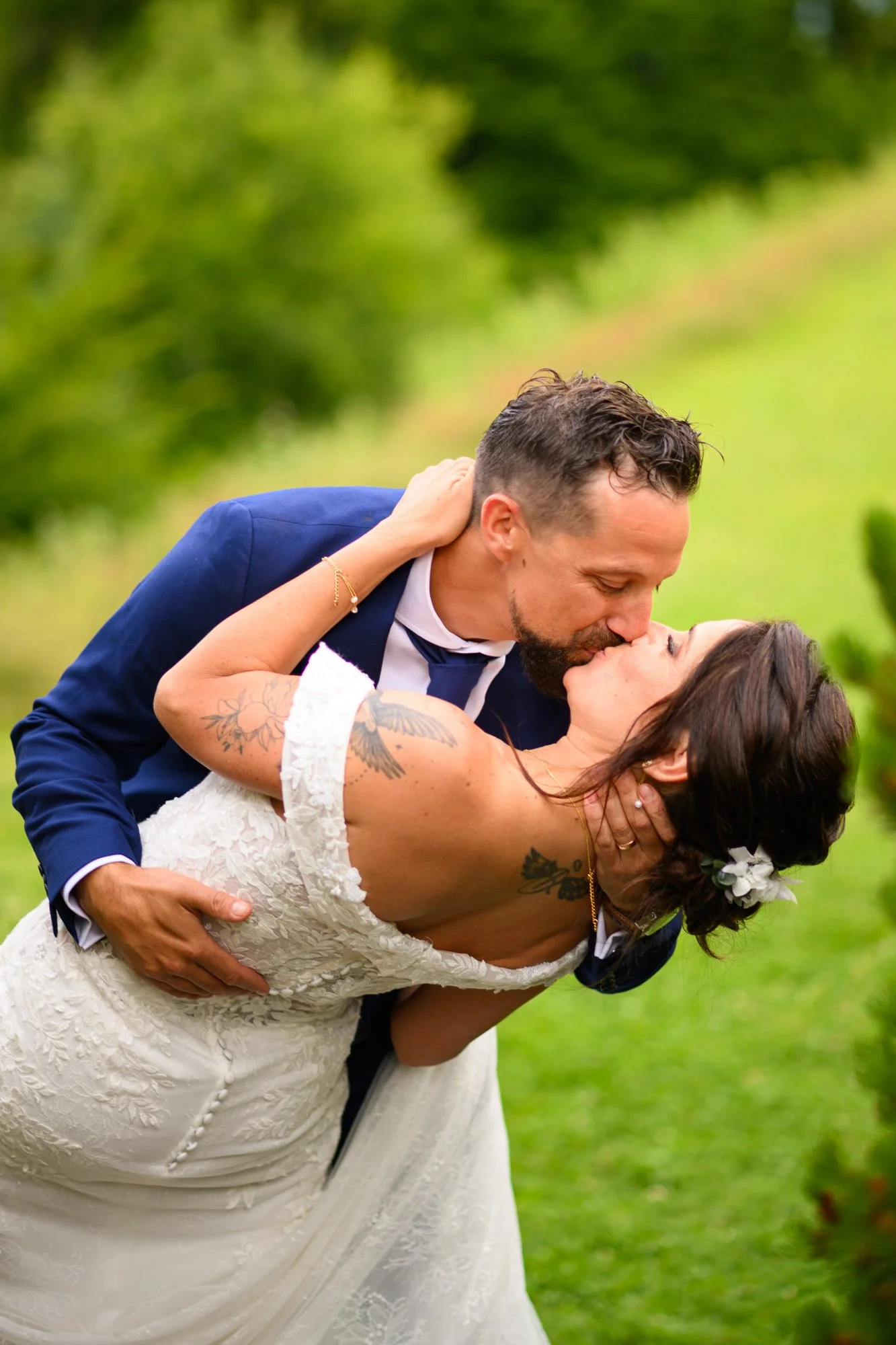 Un couple en vêtements de mariage partage un baiser dans une végétation verte.