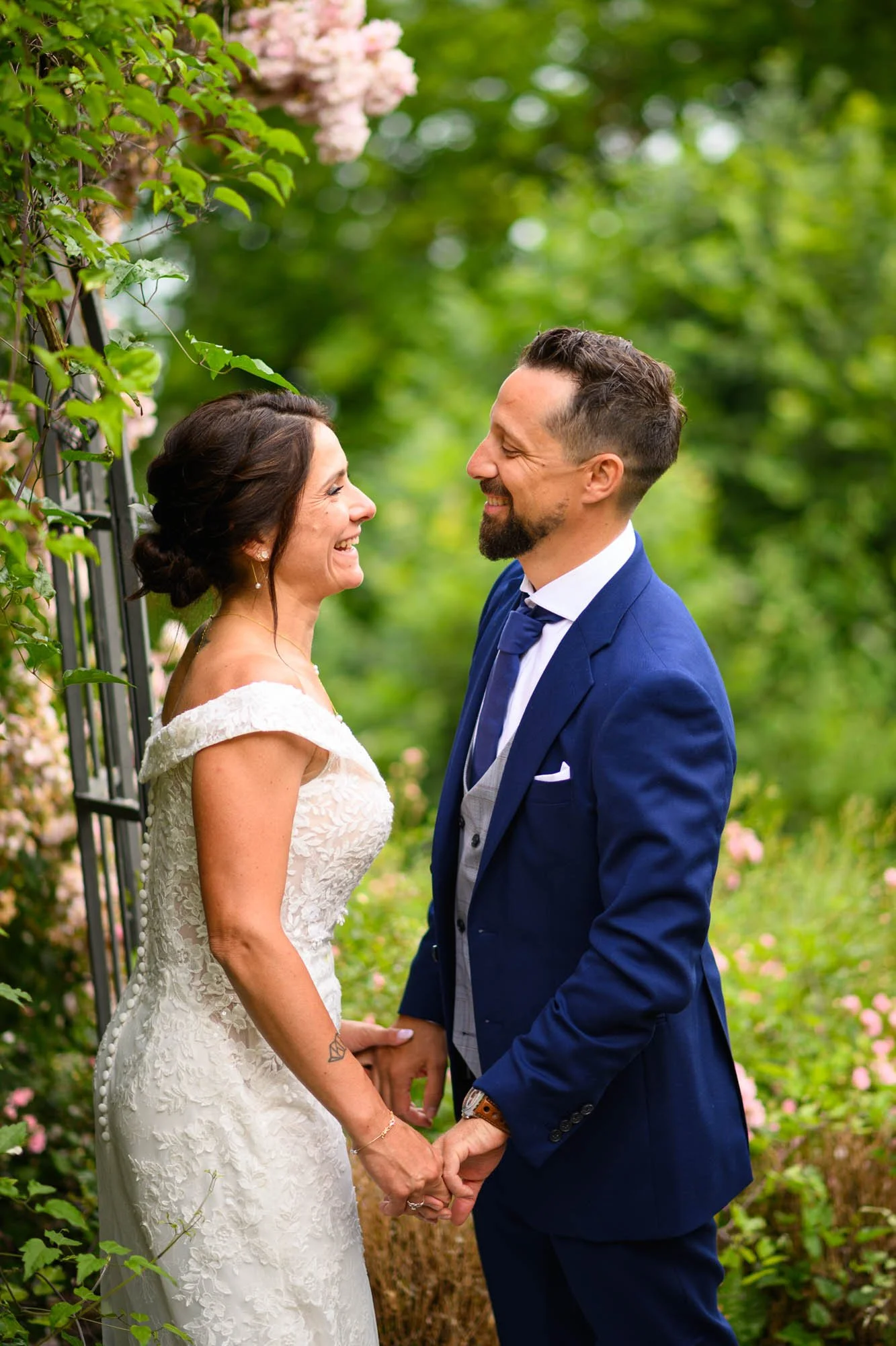 Un couple en mariage face à face, tenant leurs mains, dans un jardin fleuri verdoyant.