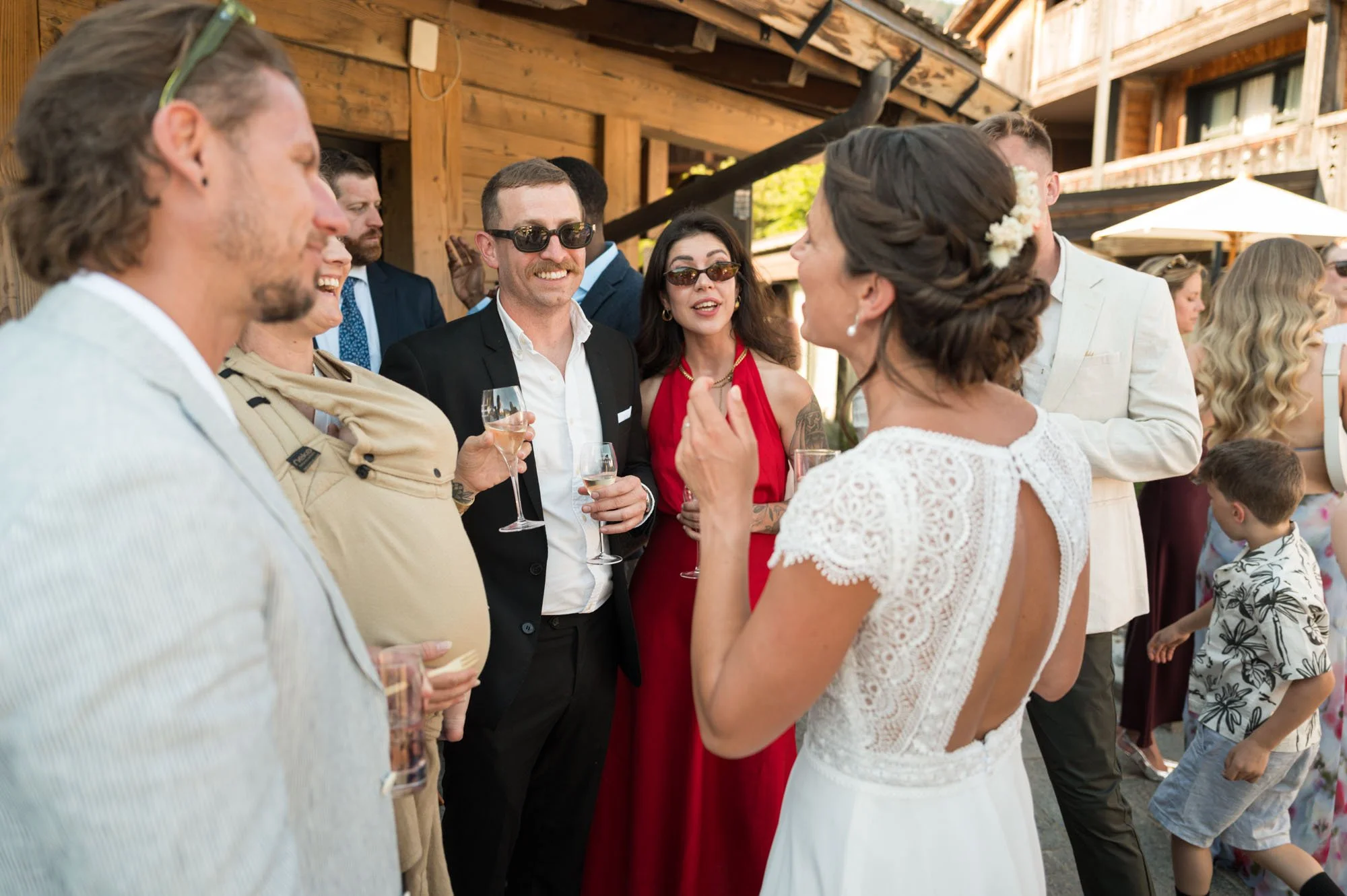 Groupe de personnes lors d'une wedding reception, discutant et tenant des verres de champagne, dans une ambiance conviviale à l'extérieur.