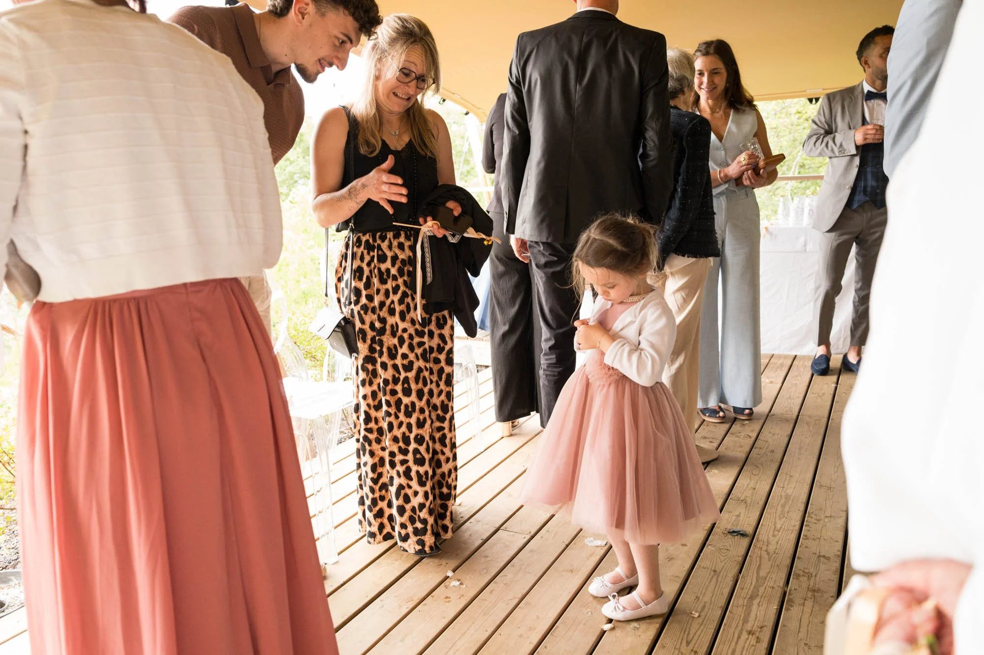 Enfants et adultes vêtus de tenues élégantes lors d'une réception en plein air sur une terrasse en bois.