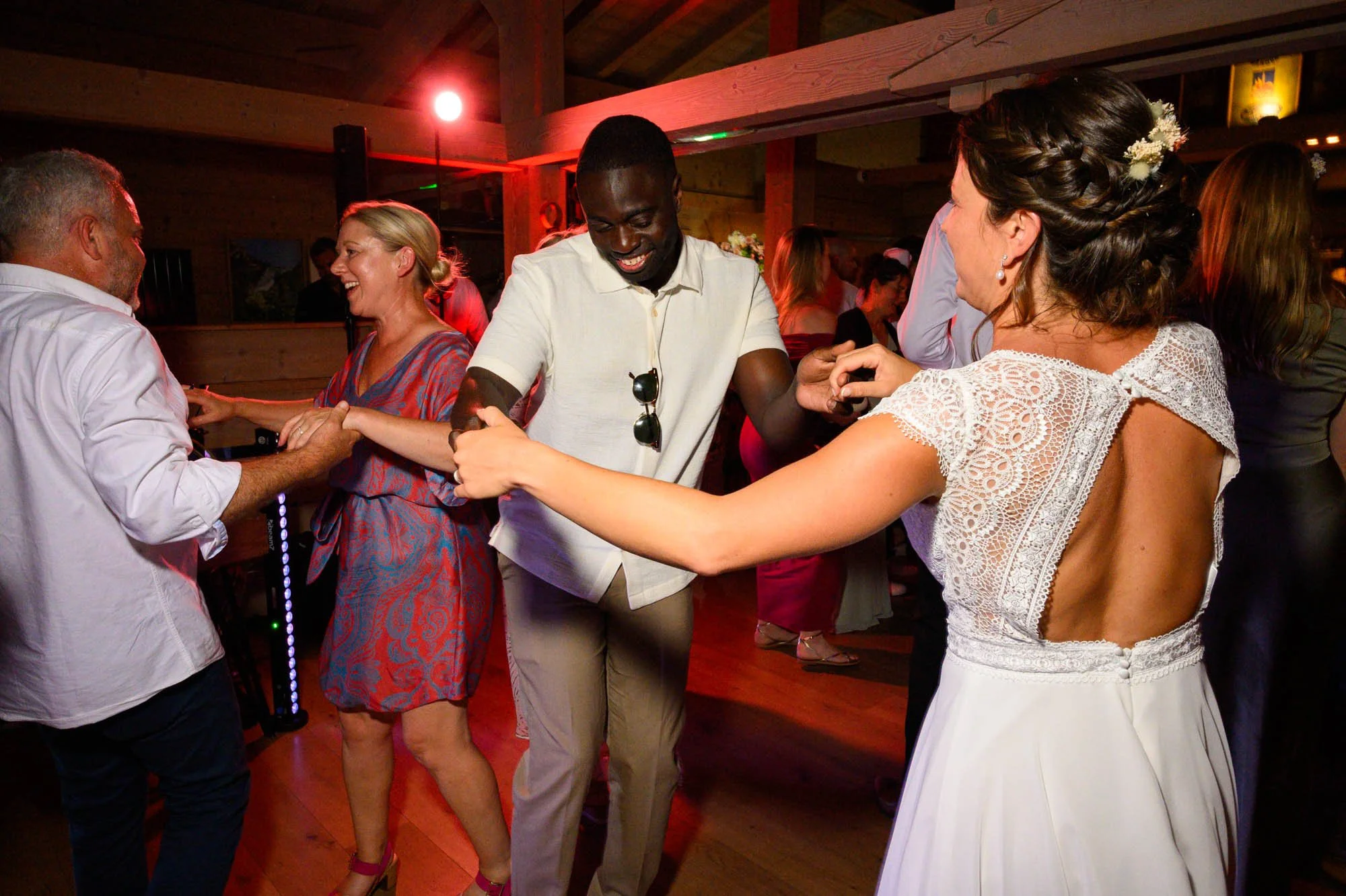 Groupe de personnes dansant lors d'une fête ou mariage, souriant et tenant les mains, ambiance chaleureuse avec éclairage doux.