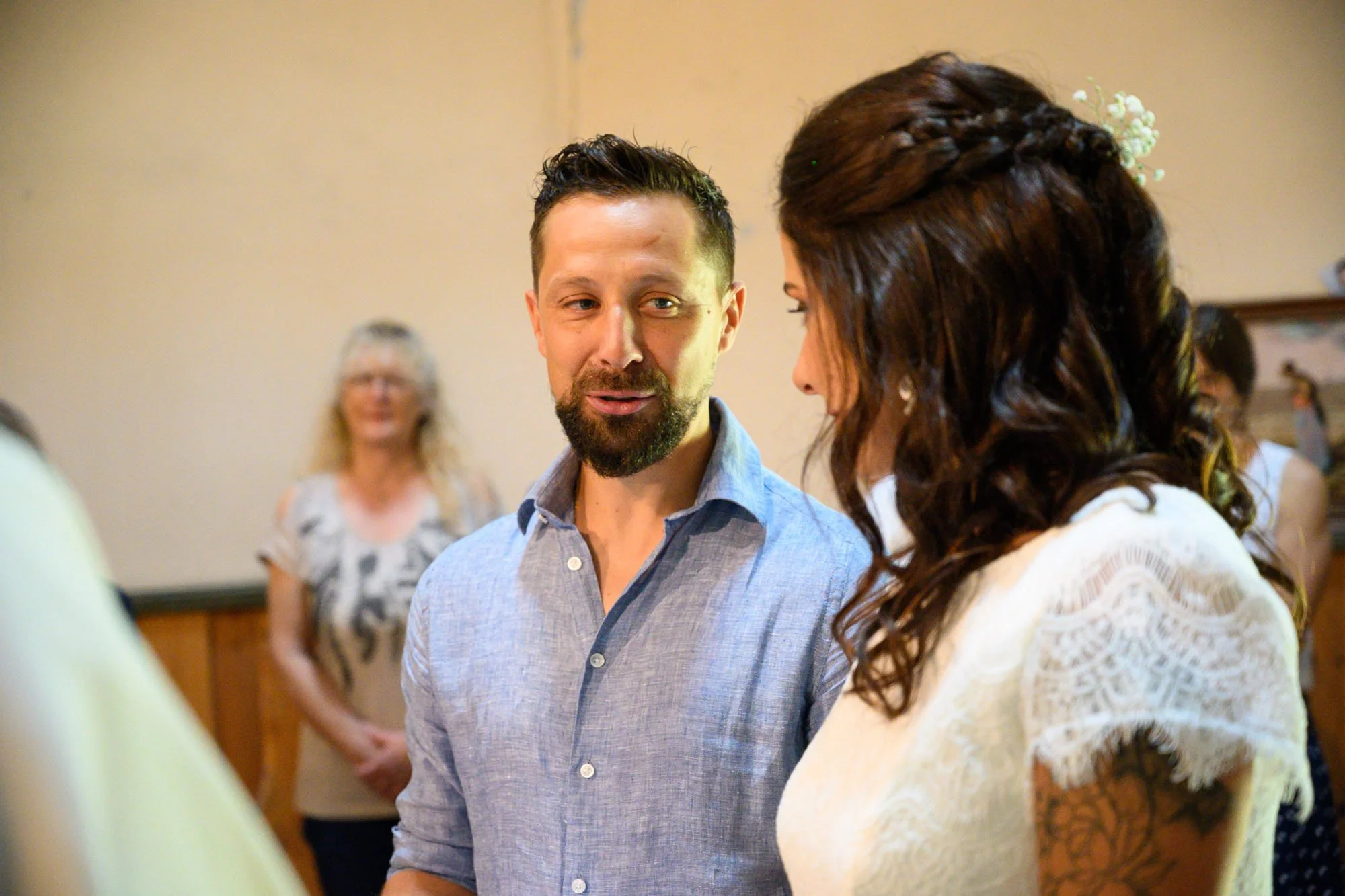 Un homme et une femme discutant lors d'une cérémonie ou d'un événement social, avec d'autres personnes en arrière-plan.