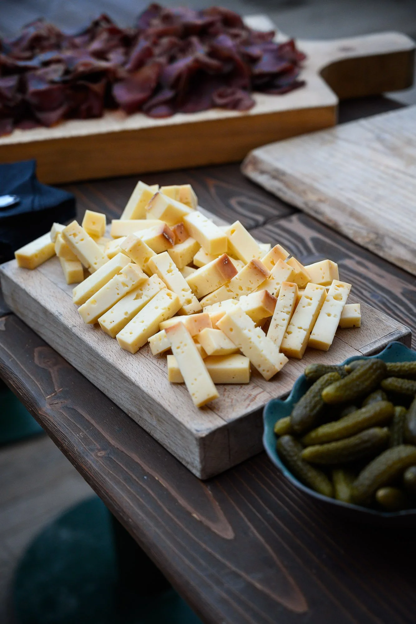 Plate de fromage coupé en morceaux, olives en conserve dans un bol, et viande à l'arrière sur une planche en bois