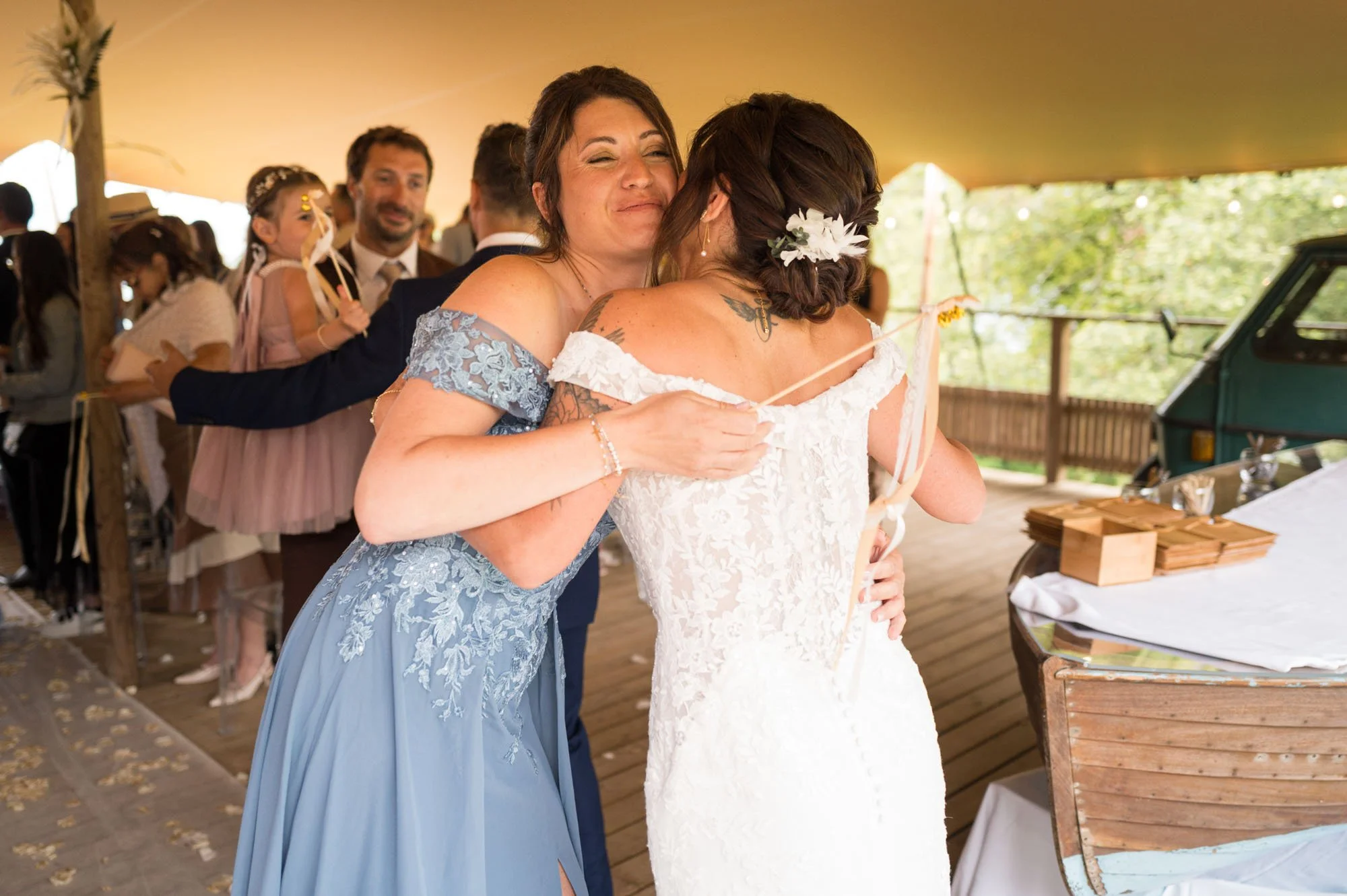 Deux femmes qui s'embrassent lors d'une célébration de mariage, entourées d'invités sous une tente décorée.