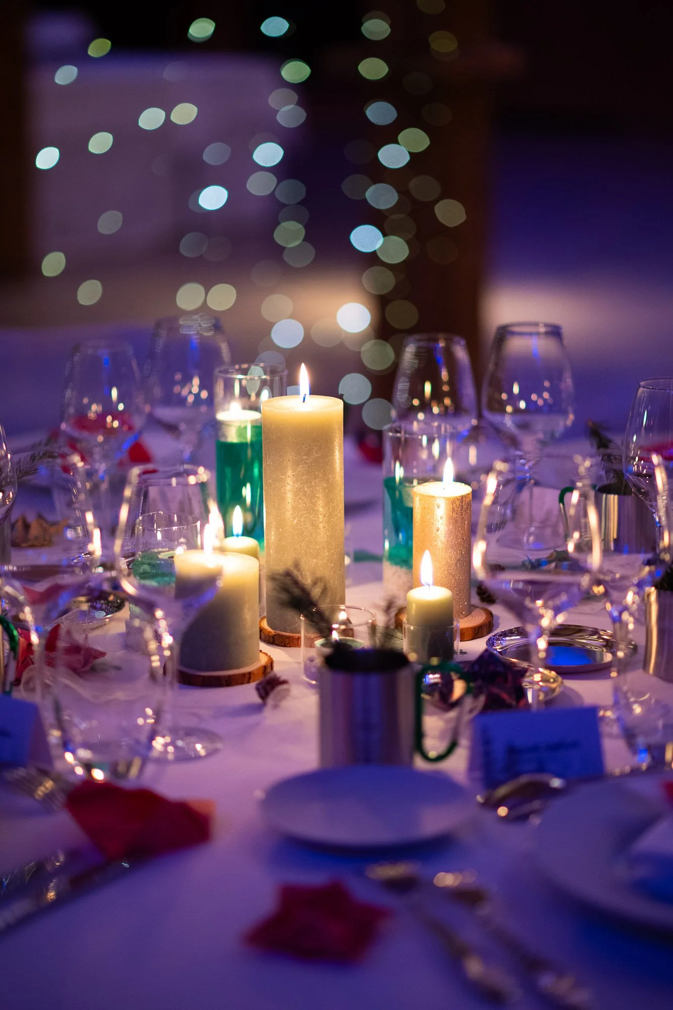 Table de fête ornée de bougies allumées, verres à vin, assiettes, et décorations, ambiance chaleureuse avec lumières bokeh en arrière-plan.