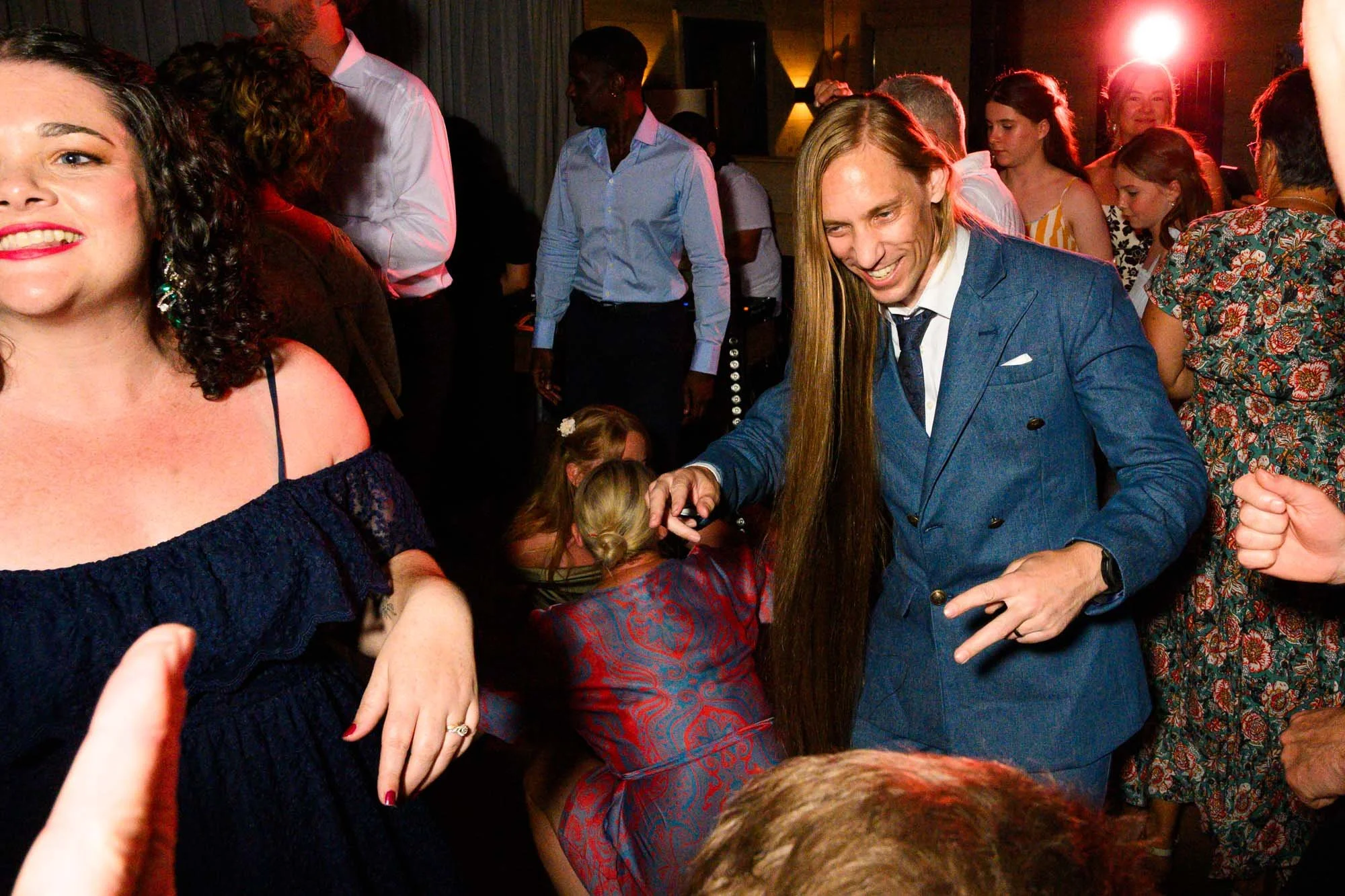 Groupe de personnes souriantes et souriantes dans une fête ou un événement social, certains dansent et d'autres discutent, ambiance festive avec éclairage chaud.