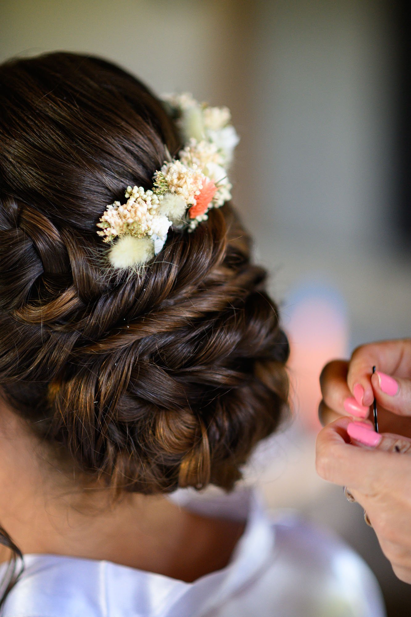 Une femme prépare ses cheveux pour un événement spécial, portant une couronne de fleurs blanches, roses et autres dans ses cheveux brun foncé.