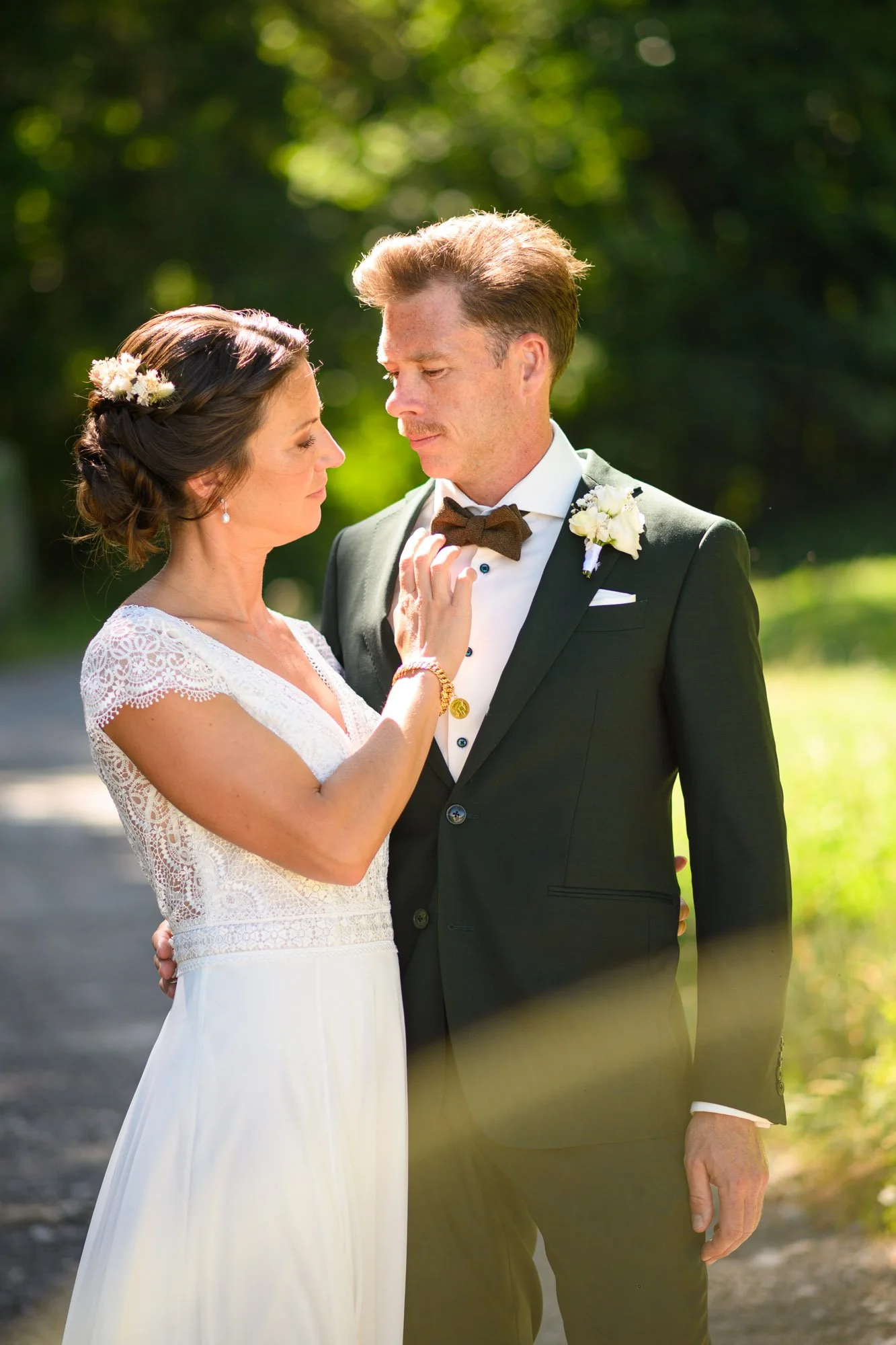 Un couple en tenue de mariage se regarde tendrement à l'extérieur, dans un environnement naturel avec des arbres en arrière-plan.