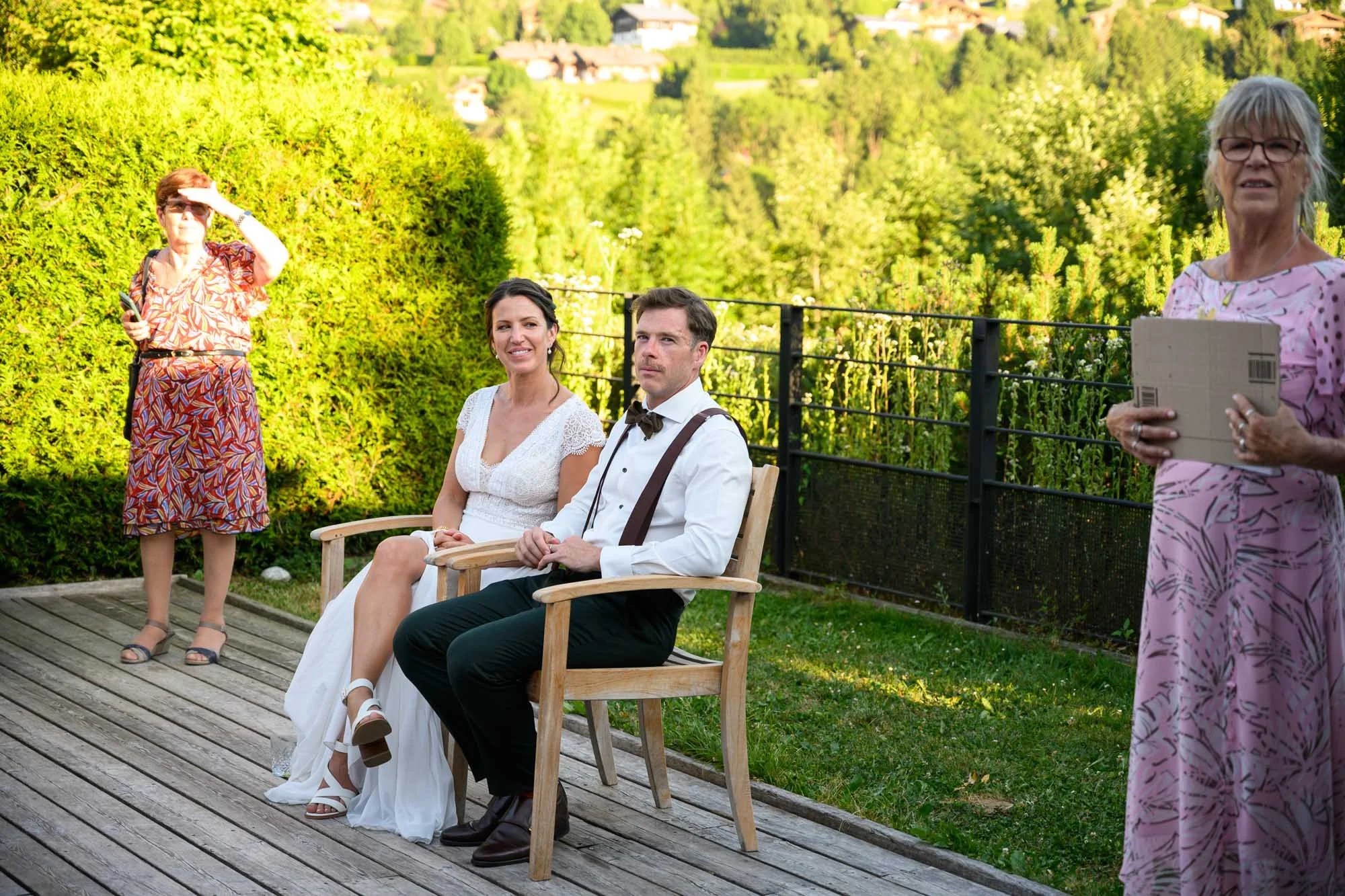 Un couple assis sur une balançoire en bois lors d'une célébration en extérieur, entouré de trois femmes, avec un paysage verdoyant en arrière-plan.