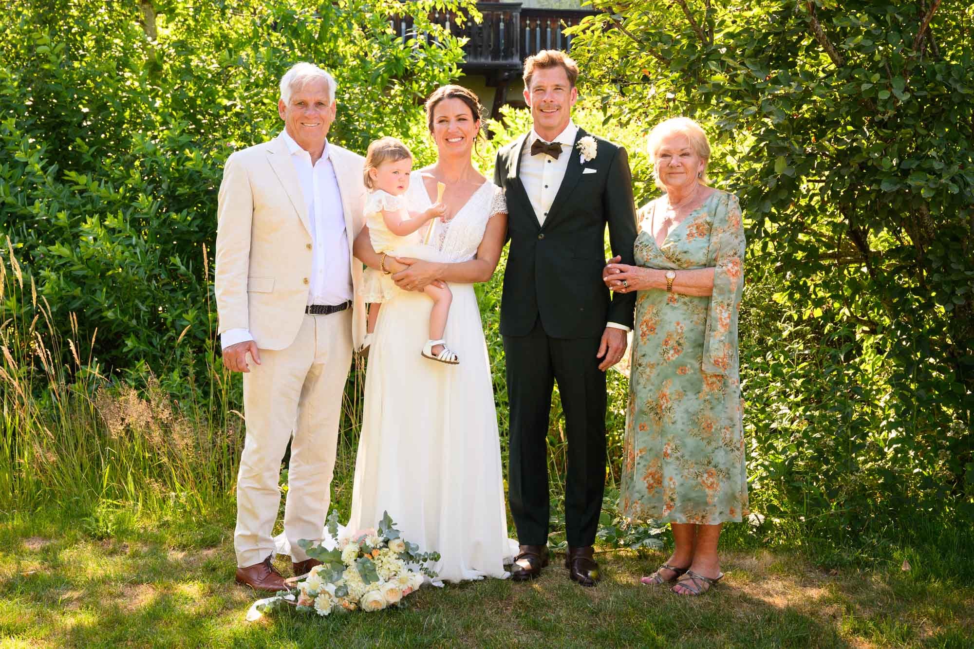 Groupe de six personnes posant à un mariage en plein air, avec des fleurs blanches au sol.