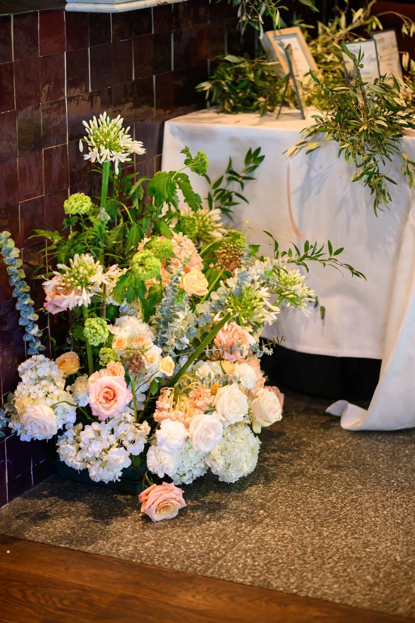 Arrangement floral avec roses pâles, hortensias blanches, et feuillage vert sur un tapis de pierre dans un espace intérieur